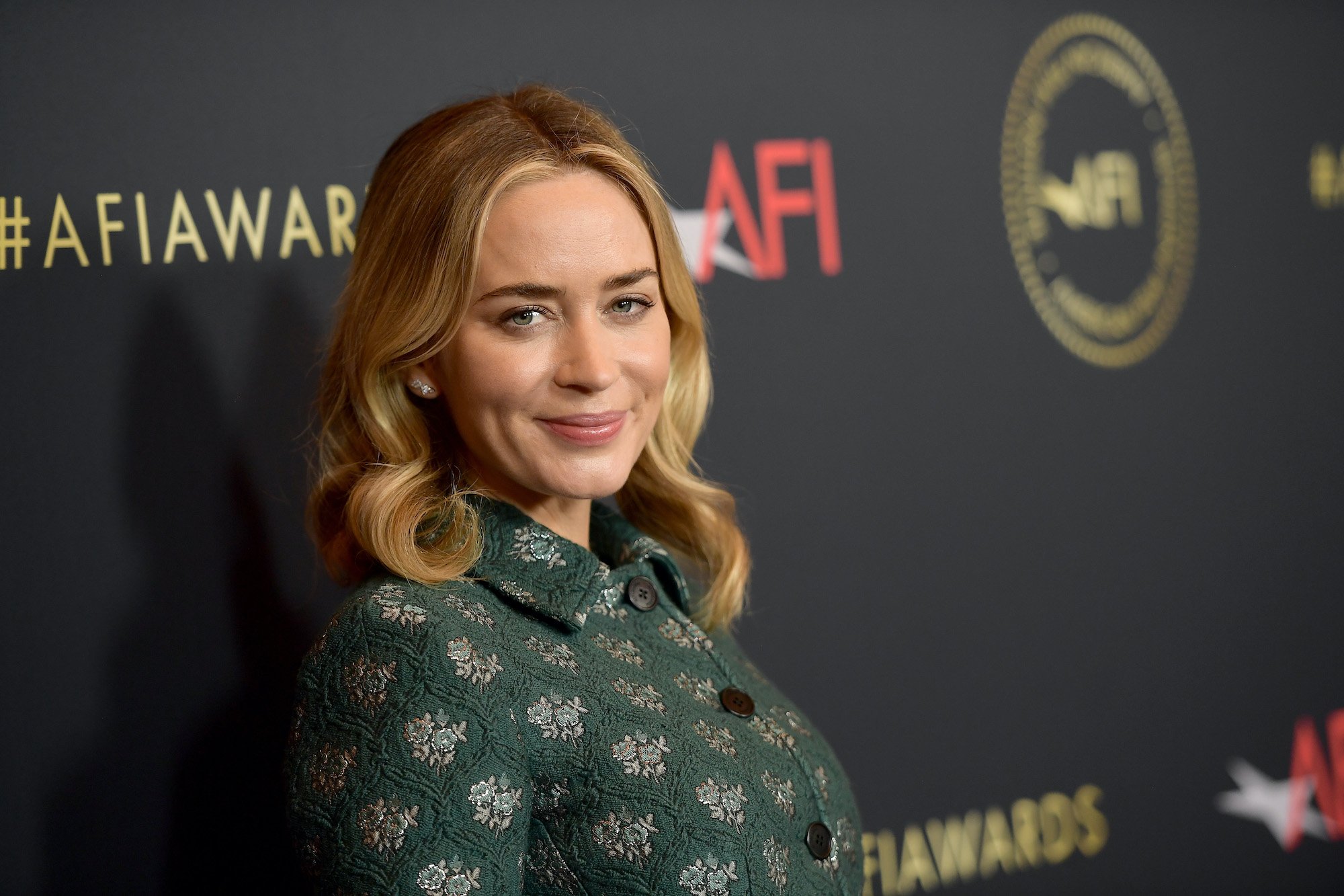 Emily Blunt smiling in front of a black background