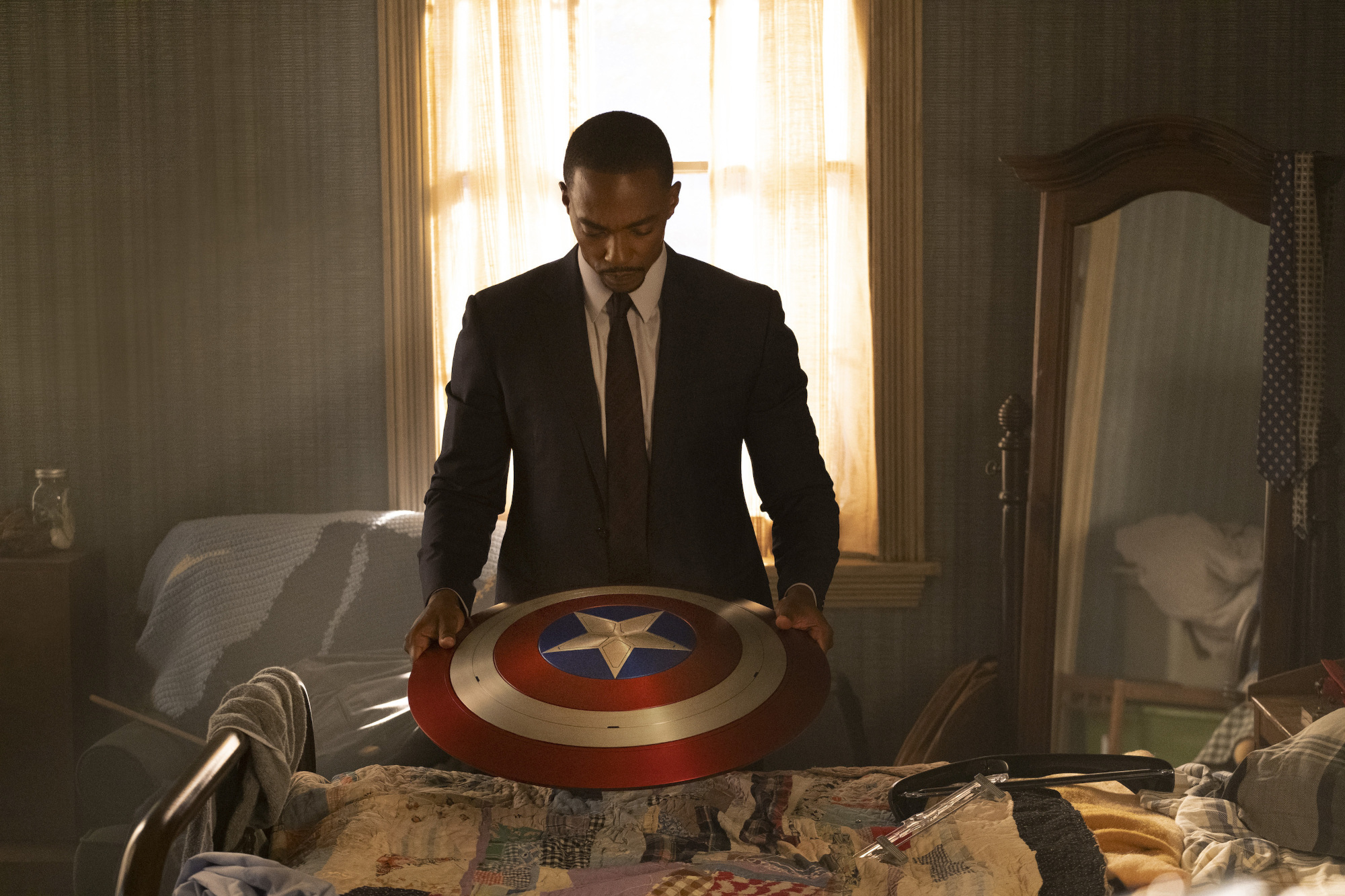 Anthony Mackie as Sam Wilson in 'The Falcon and the Winter Soldier' Episode 1. Captain America's shield sits on a desk, and he's standing behind the desk and looking down at it.