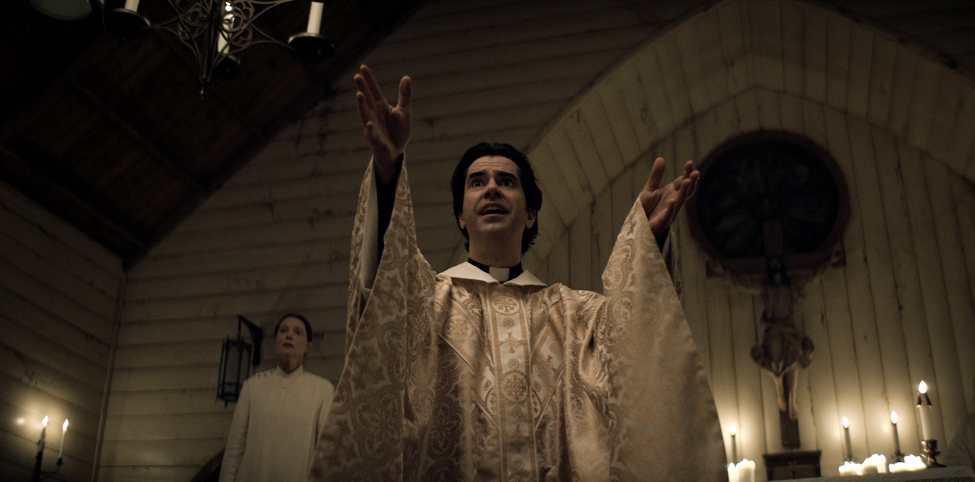 Samantha Sloyan as Bev Keane, with Hamish Linklater in 'Midnight Mass' as Father Paul with his hands in prayer walking down the aisle in the Crockett Island Church