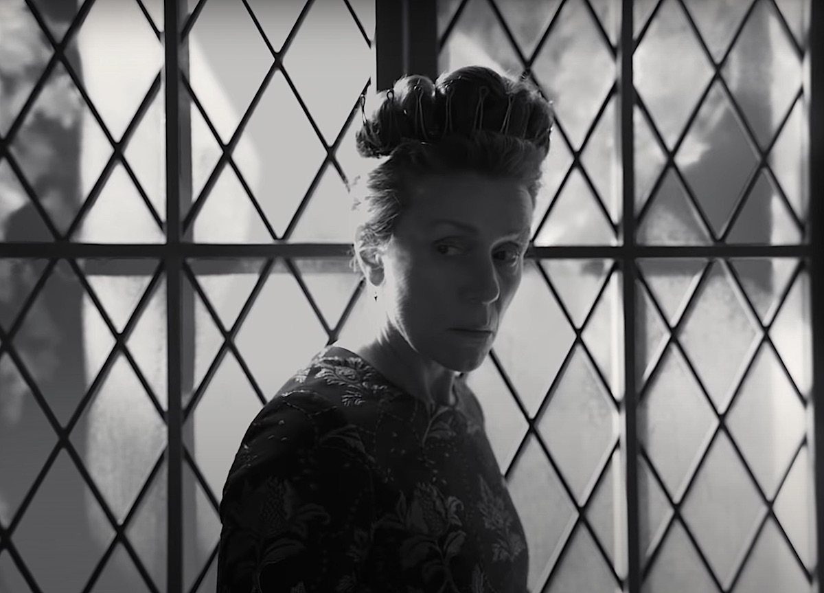 Frances McDormand as Lady Macbeth in 'The Tragedy of Macbeth' trailer. In the black-and-white photo, McDormand wears a dark dress with floral embellishments with her hair done up high and a crown circling it. She stands in front of a large window with diamond lattice and looks concerned. McDormand co-stars in the film with Denzel Washington, who plays Lord Macbeth. 'The Tragedy of Macbeth' comes out Dec. 25 in theaters and Jan. 14 on Apple TV+. It's an A24 film written and directed by Joel Coen.