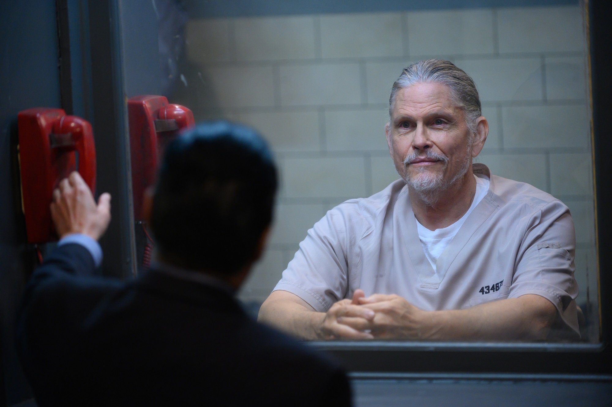 General Hospital will feature the return of Cyrus Renault, pictured here in a grey prison jumpsuit while looking through a plexiglass