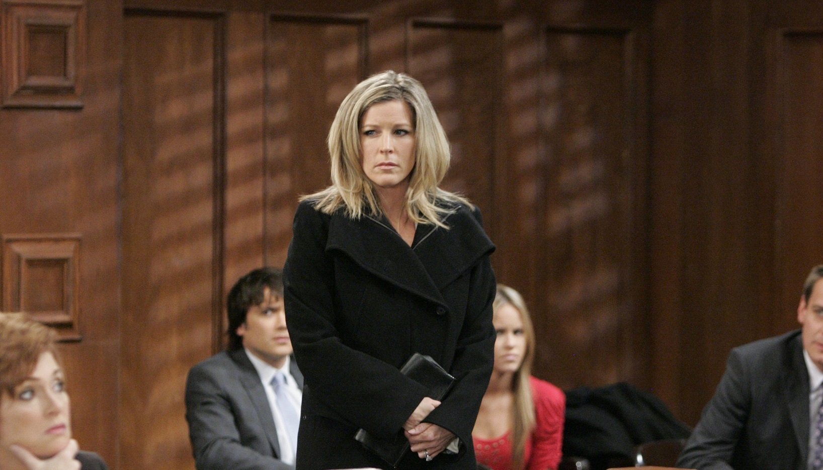 General Hospital comings and goings focus on Carly's wedding to Jason. Carly is pictured in a courtroom, in a Black shirt with a black peacoat over it.