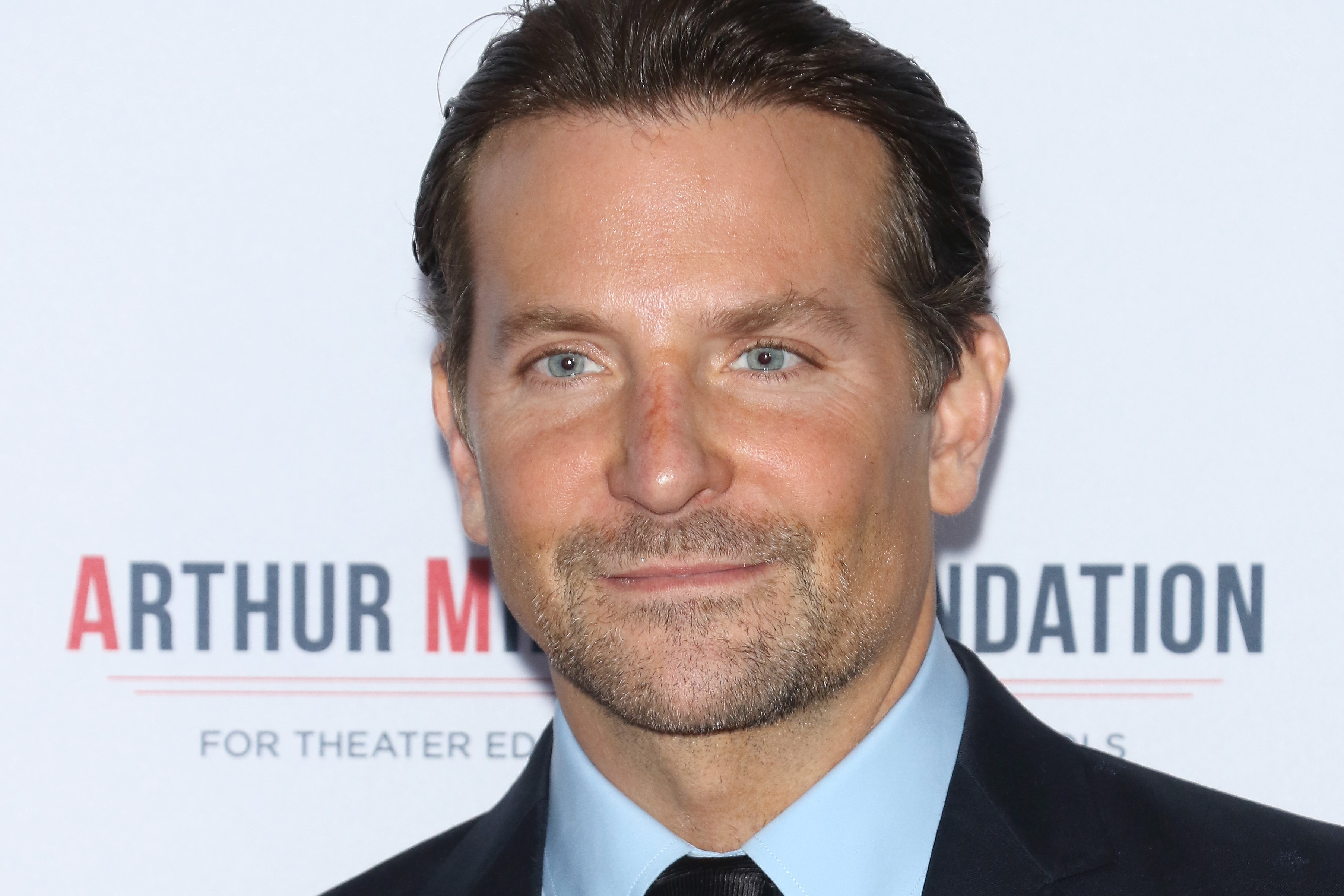 Bradley Cooper, in  a black suit and sky blue shirt, at an event in 2019.