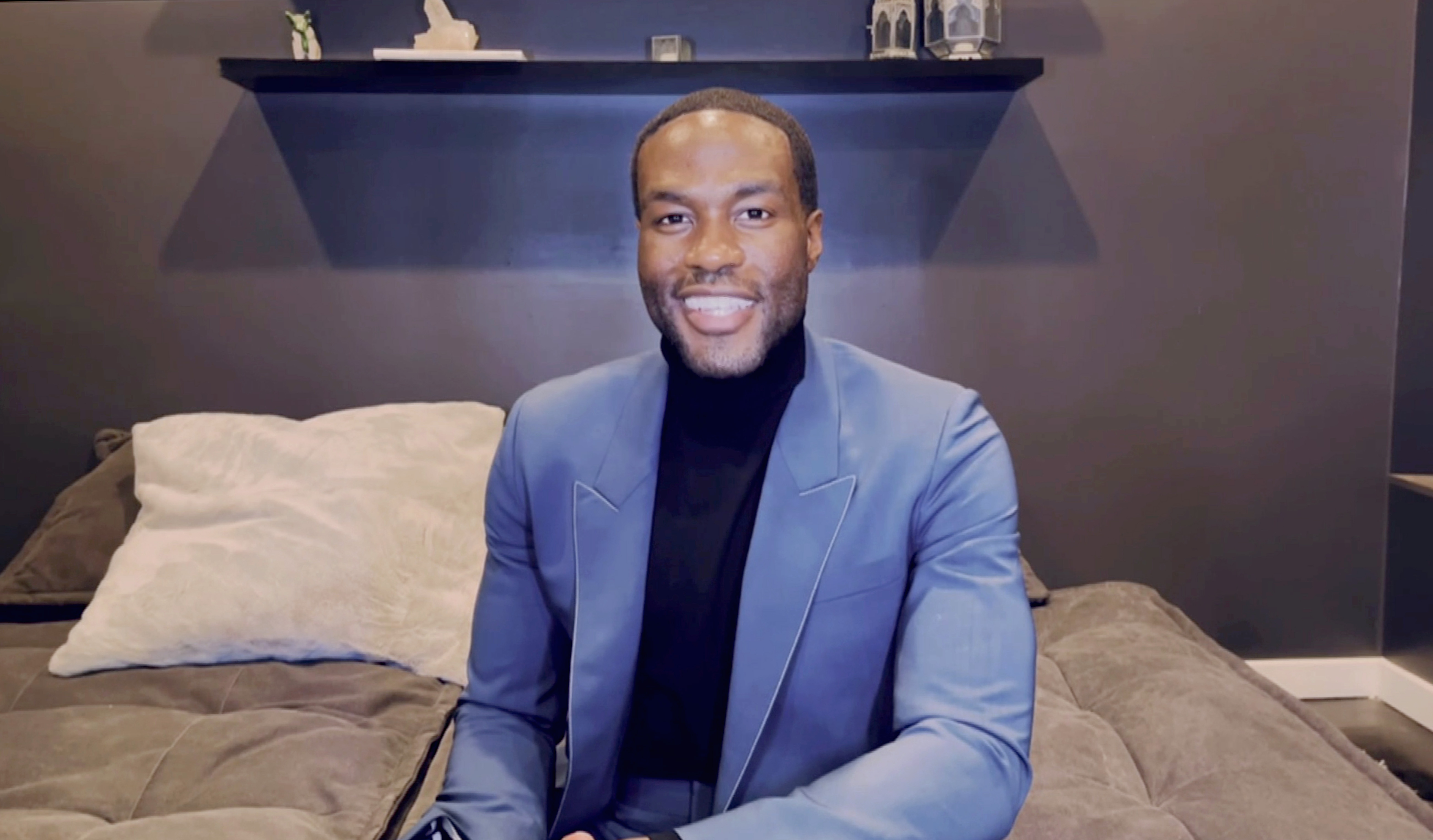 Yahya Abdul-Mateen II smiles wearing a blue jacket and black shirt.