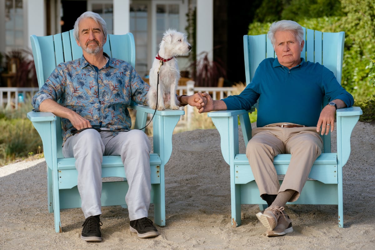 Robert and Sol sit in chairs in front of the beach house holding hands in Grace and Frankie. Sol's dog sits next to him on the arm of the chair.