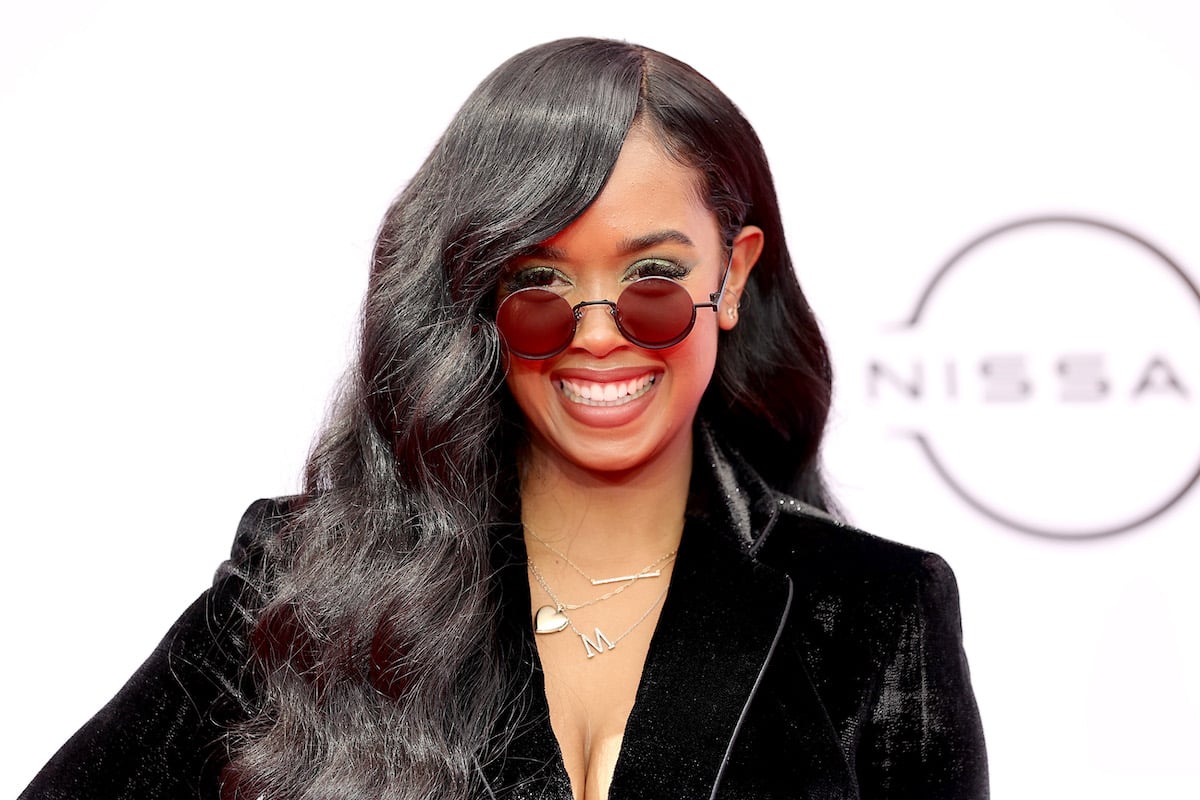 H.E.R. wearing sunglasses and smiling.