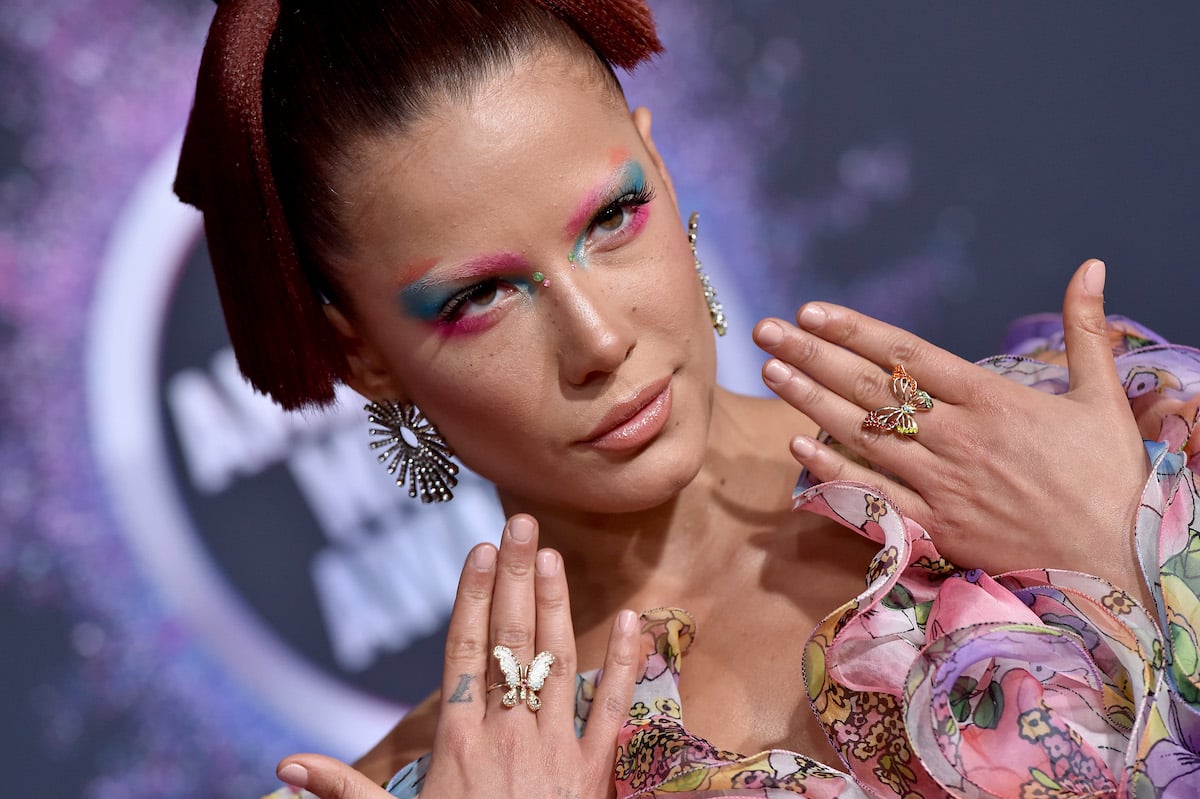 Halsey wearing elaborate makeup poses with her hands up at an event.