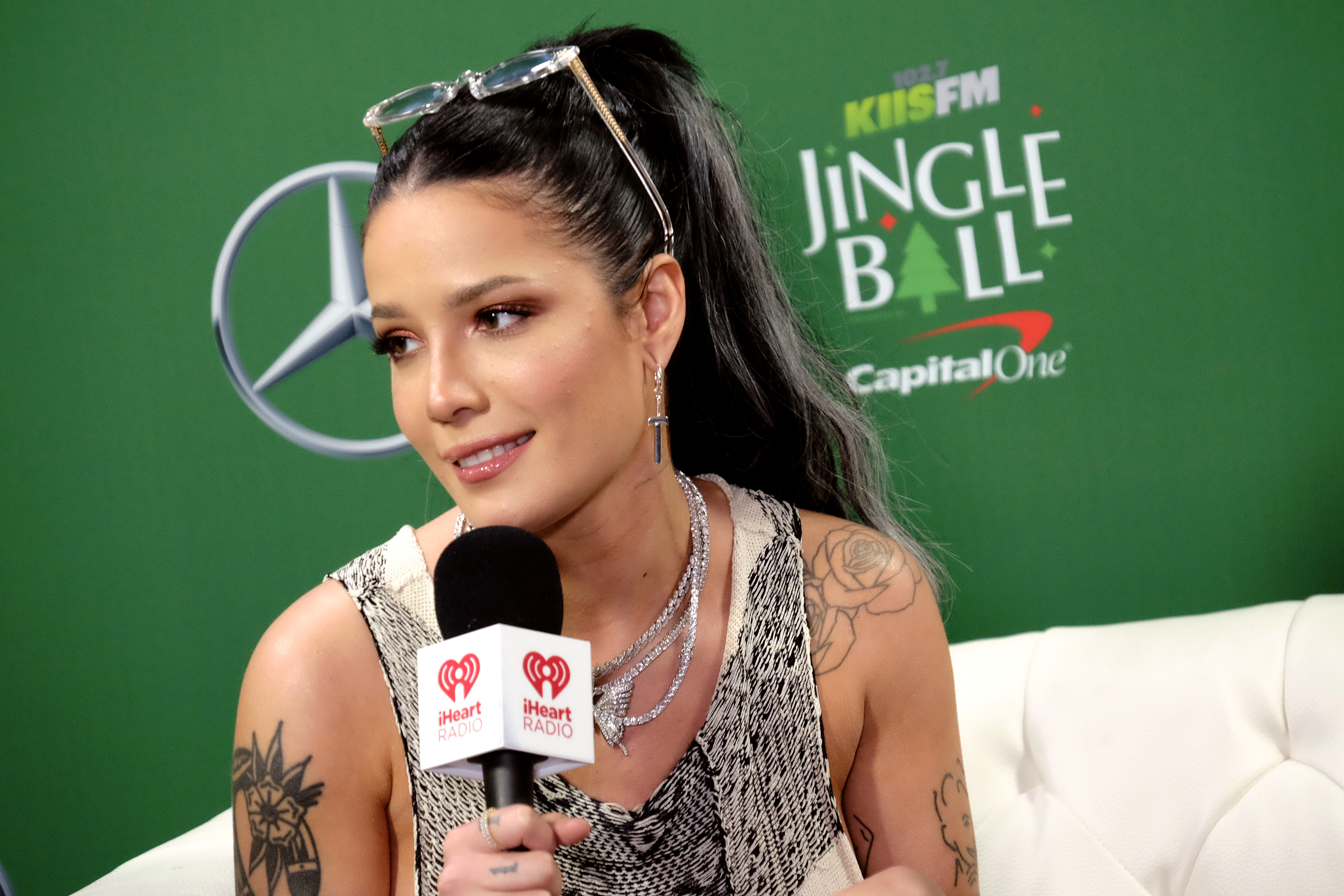 Halsey holds a microphone while sitting on a white couch at 102.7 KIIS FM's Jingle Ball 2019