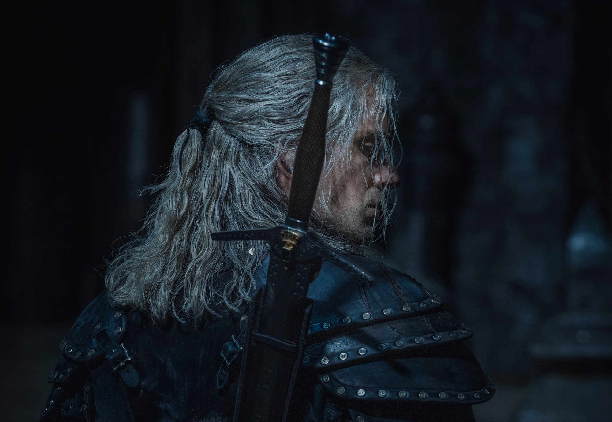 Henry Cavill as Geralt of Rivia in 'The Witcher,' which Netflix renewed for season 3. He's wearing black leather, his blonde hair is half-up, and he's turned away from the camera.