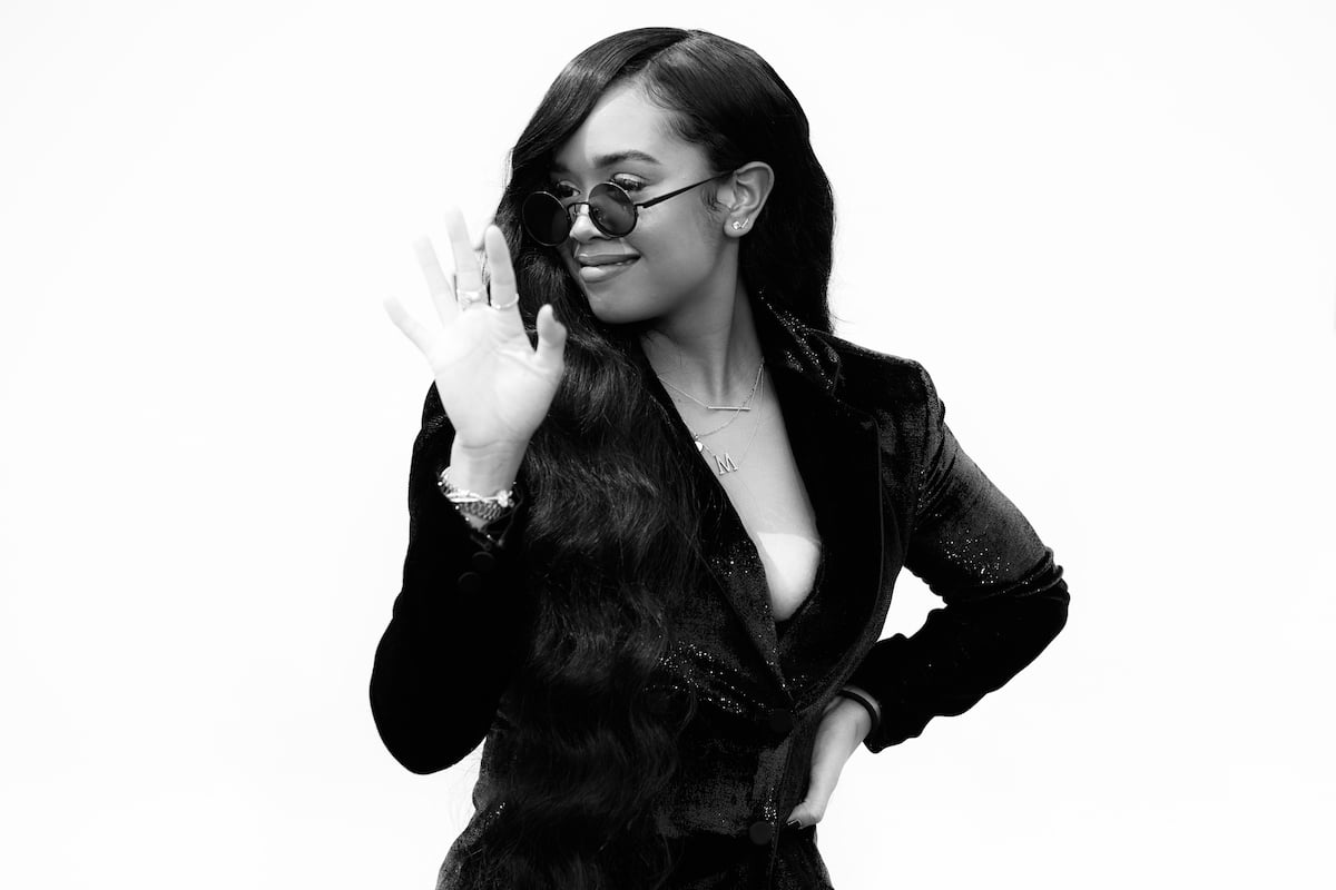 H.E.R. smiling and waving while wearing sunglasses.