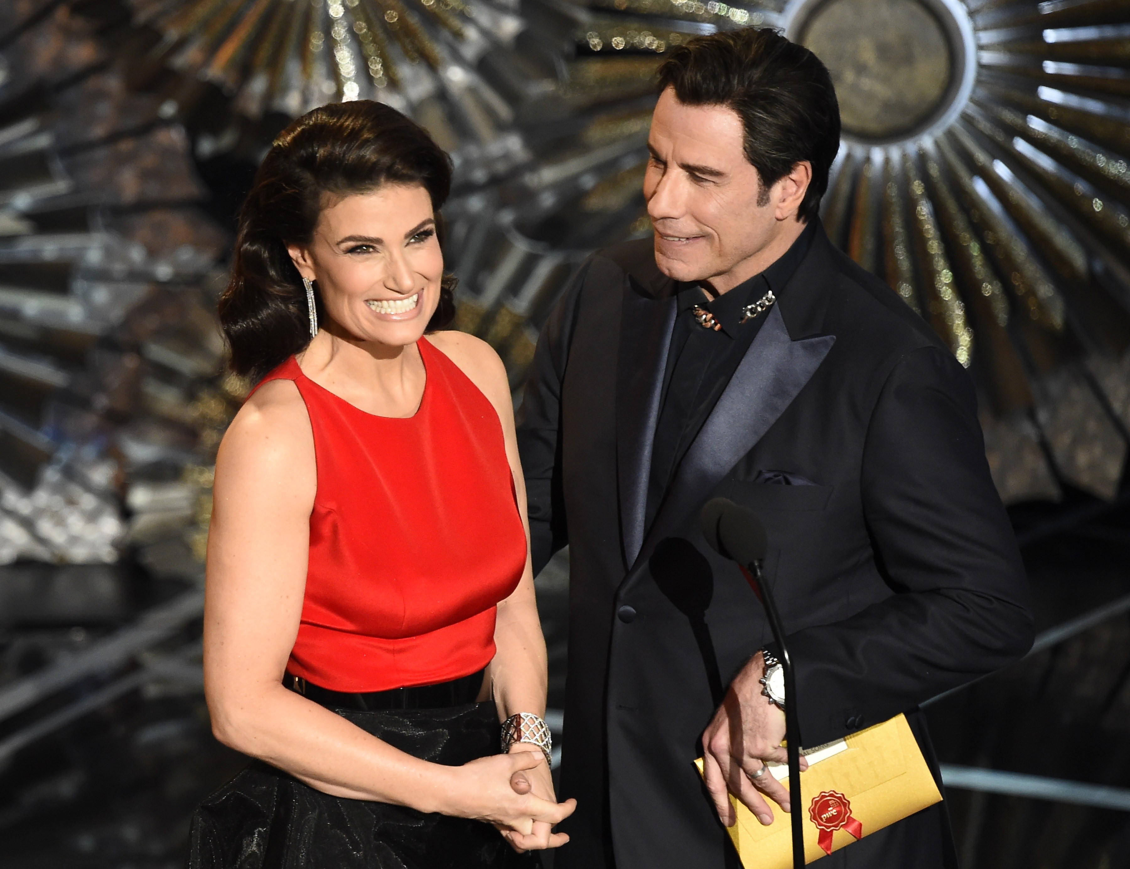 Idina Menzel in a red dress and John Travolta in a black suit on stage at the Oscars. 