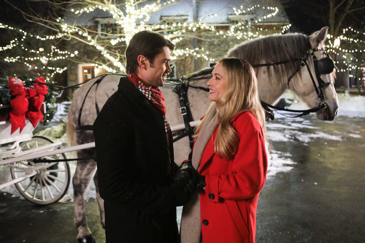 Man and woman standing in front of a horse-drawn carriage in Lifetime Christmas movie 'It Takes a Christmas Village'
