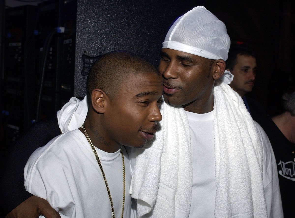 Ja Rule wearing a white shirt and gold chain embraced by R. Kelly wearinga  white shirt with a white towel around his neck.