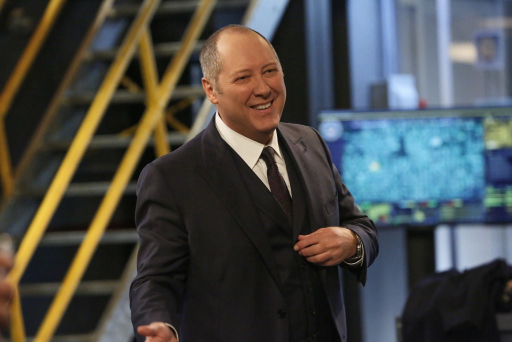 James Spader as Raymond 'Red' Reddington in 'The Blacklist' is dressed in a dark suit while smiling in the task force room.