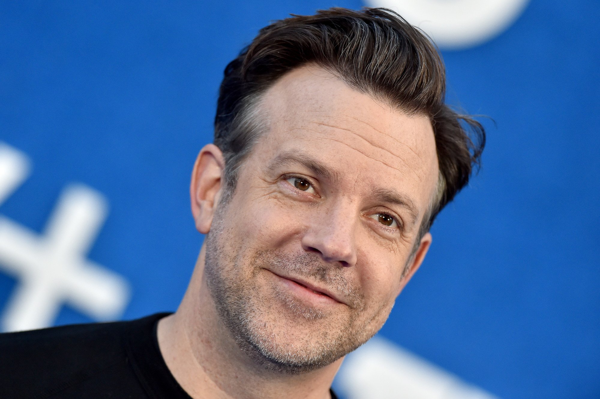 'Ted Lasso' star Jason Sudeikis, who will star in Marvel's 'Hit-Monkey' series coming to Hulu. He's wearing a black shirt, and his brown hair is slicked back.