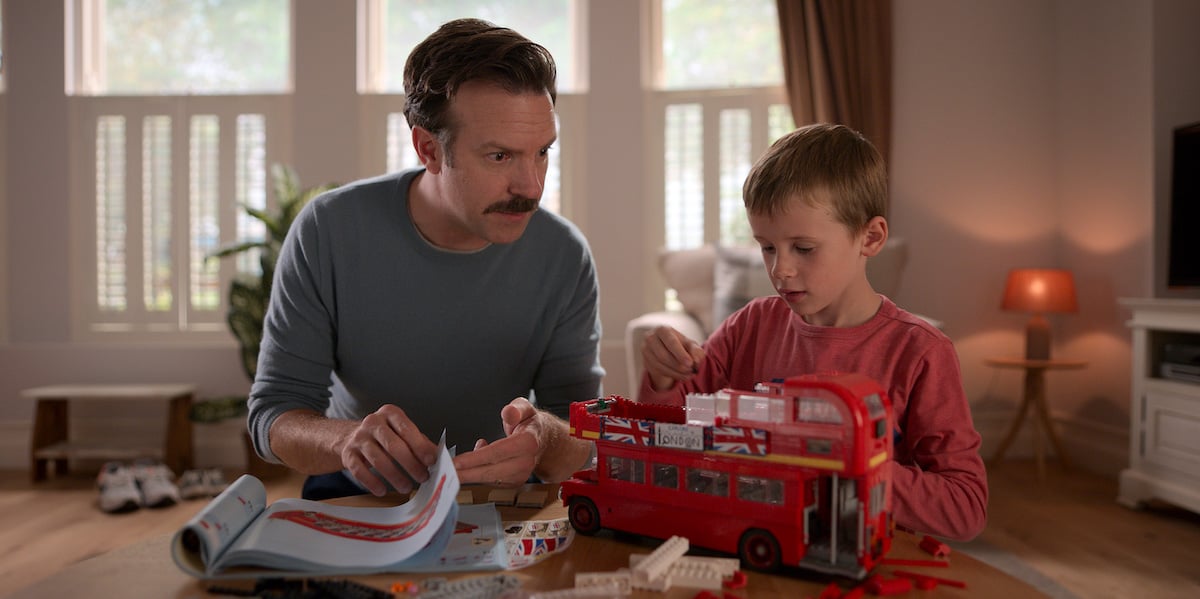 Jason Sudeikis watches as Gus Turner assembles a red double decker bus in 'Ted Lasso'