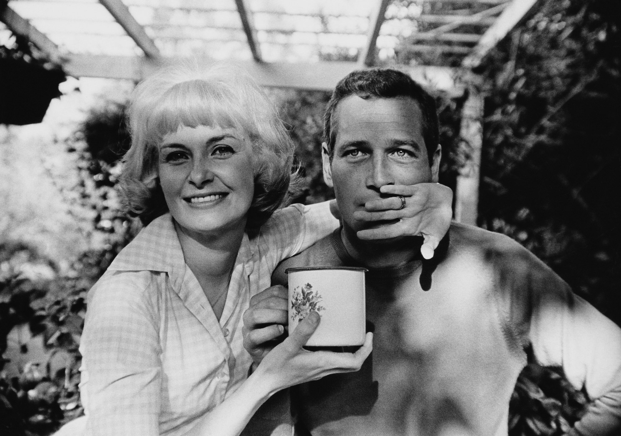 smiles and blocks her husband Paul Newman's face while holding a coffee mug