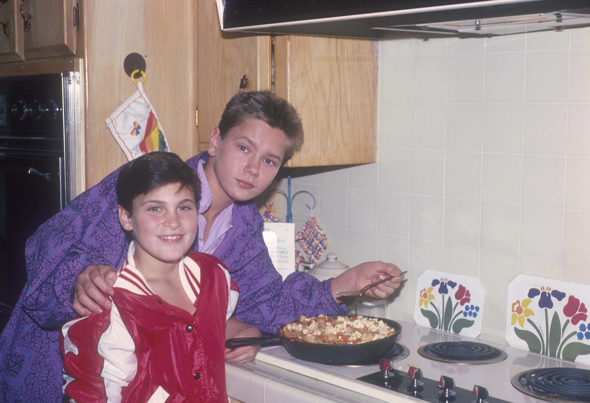 Joaquin and River Phoenix smiling, cooking in their home, 1985