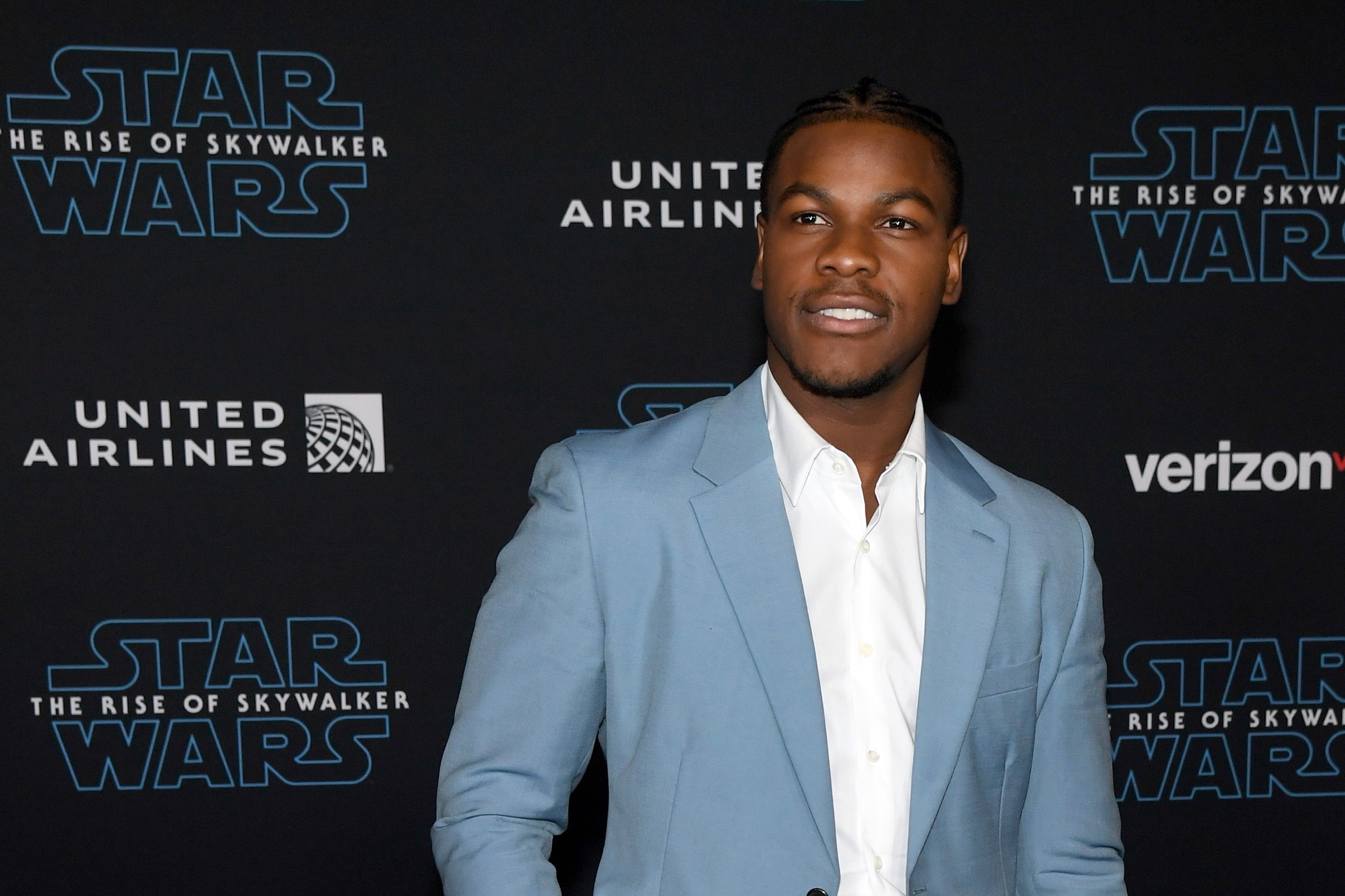John Boyega, in a light blue suit jacket and white shirt, at the premiere of Disney's 'Star Wars: The Rise of Luke Skywalker' in 2019.