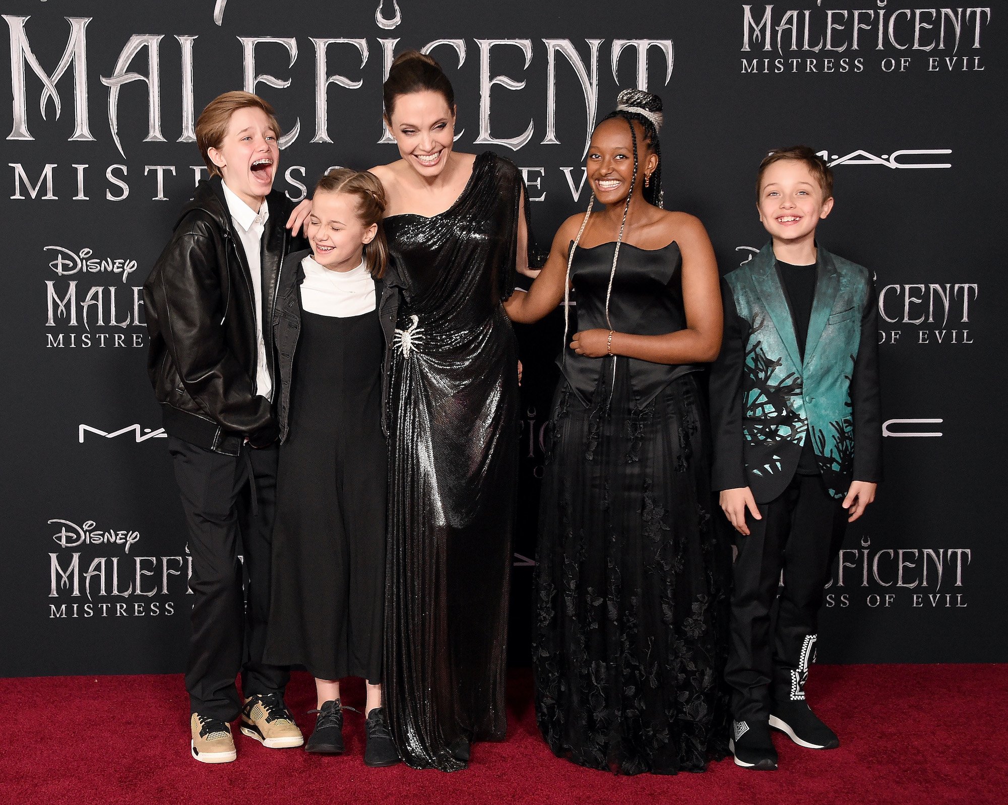 Angelina Jolie laughing with her kids in front of a black background on the red carpet