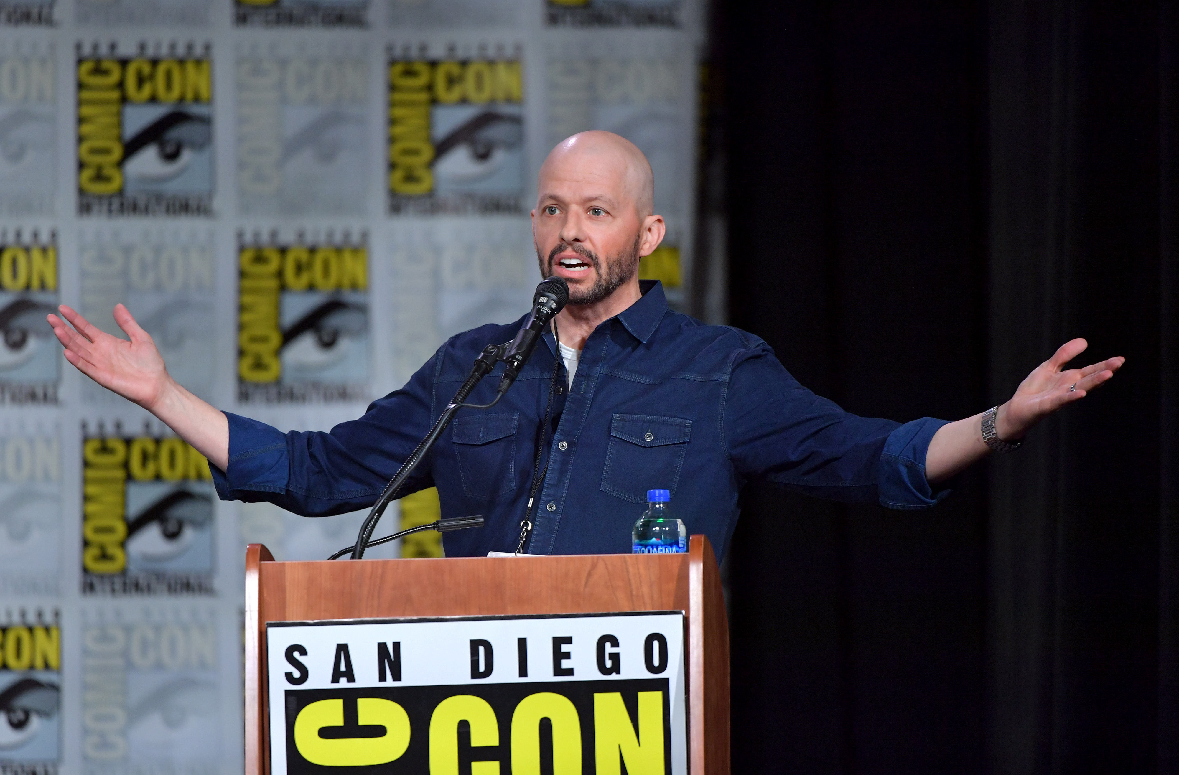 'Supergirl' actor Jon Cryer, who plays Lex Luthor, wears a dark blue jean button-down long-sleeved jacket and stands in front of a San Diego Comic-Con speaking podium.
