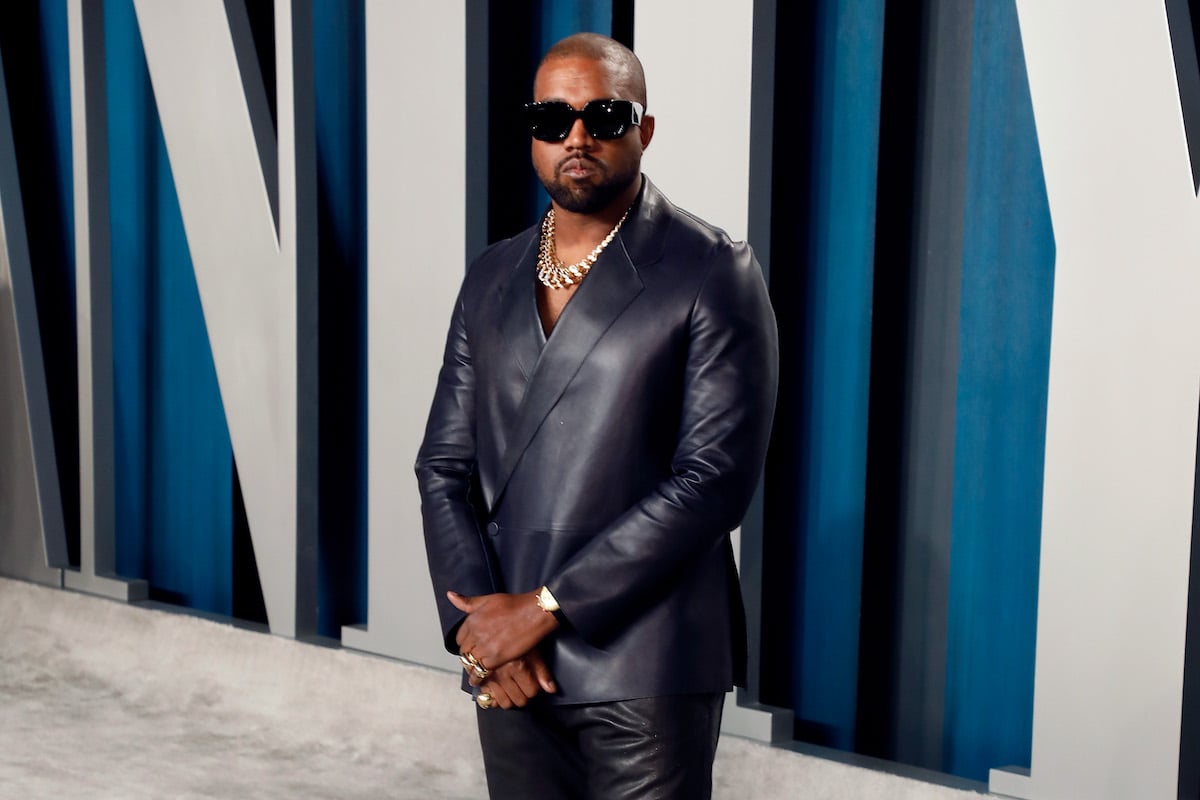 Kanye West poses in a black leather suit and black sunglasses at an event.
