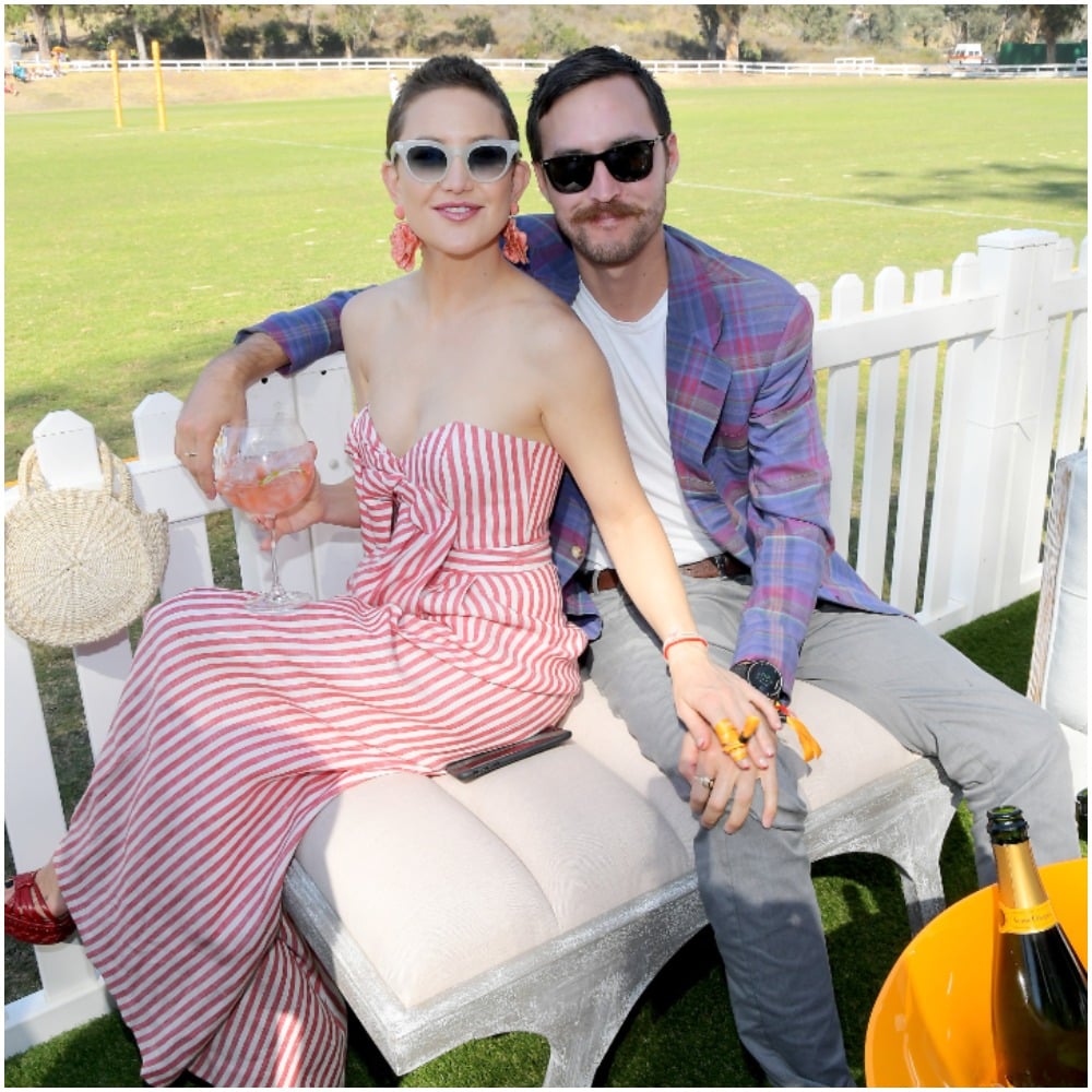 Kate Hudson and Danny Fujikawa attending the Eighth Annual Veuve Clicquot Polo Classic wearing a striped dress and patterned blazer.