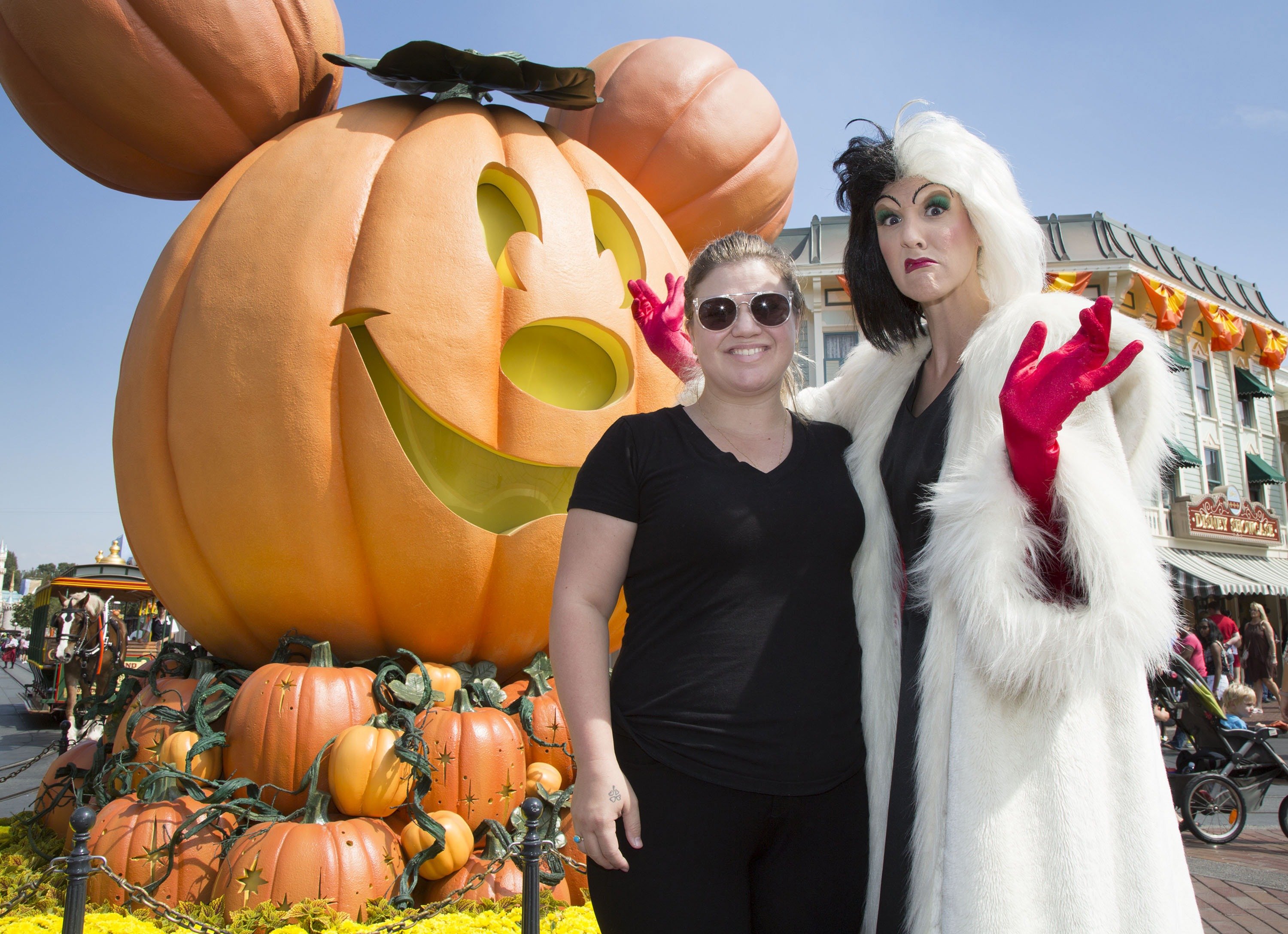 Kelly Clarkson smiles next to Disneyland's Cruella de Vil on a sunny day