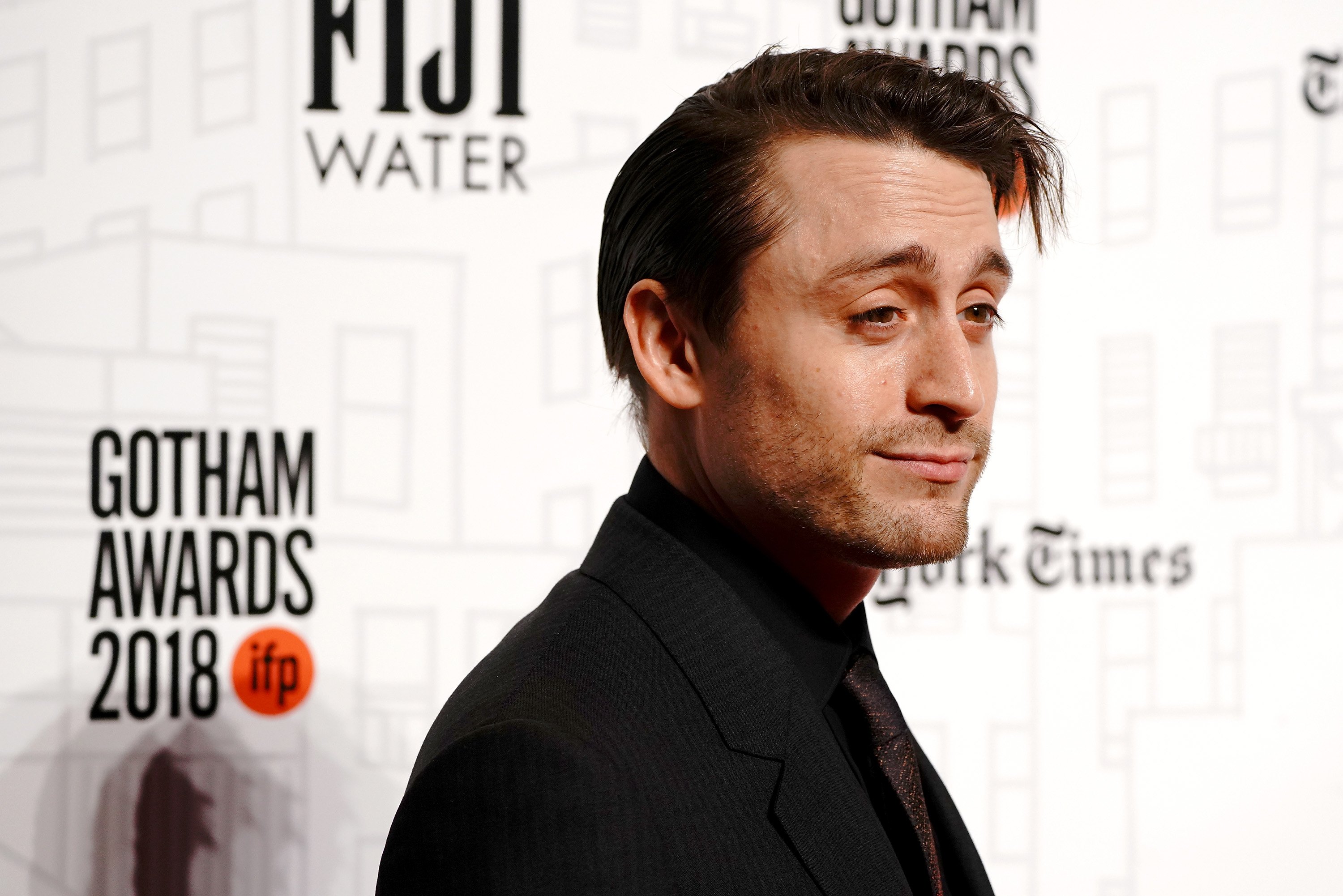 Kieran Culkin, from chest up, standing in front of a white backround with his side face toward the camera.