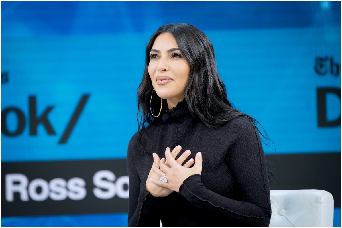 Kim Kardashian West sitting down and smiling with her hands on her chest.