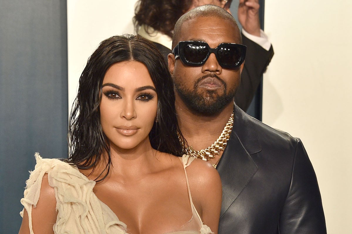 Kim Kardashian West wears a white gown and poses with Kanye West wearing dark sunglasses at an event.