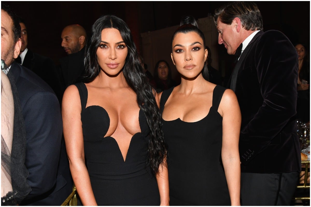 Kim Kardashian and Kourtney Kardashian wearing black designer dresses while posing on the red carpet.