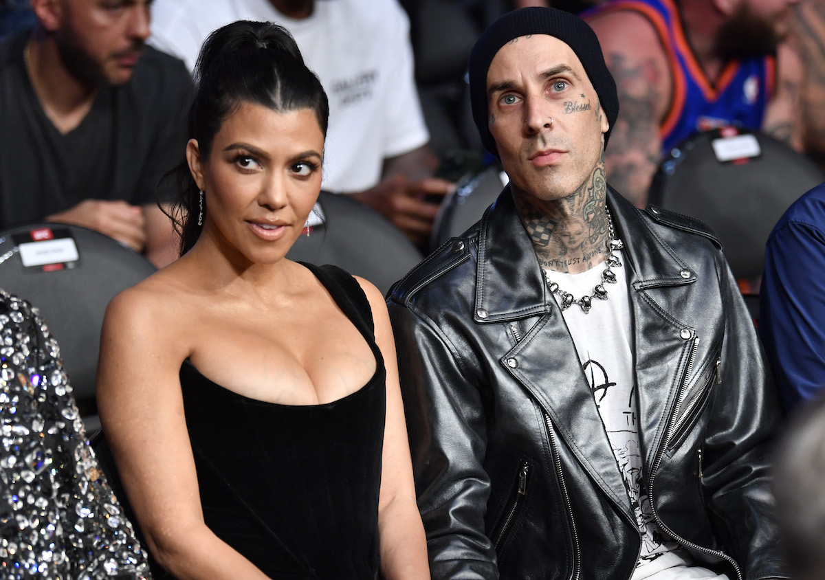 Kourtney Kardashian and Travis Barker sit together at an event with skeptical looks on their faces.