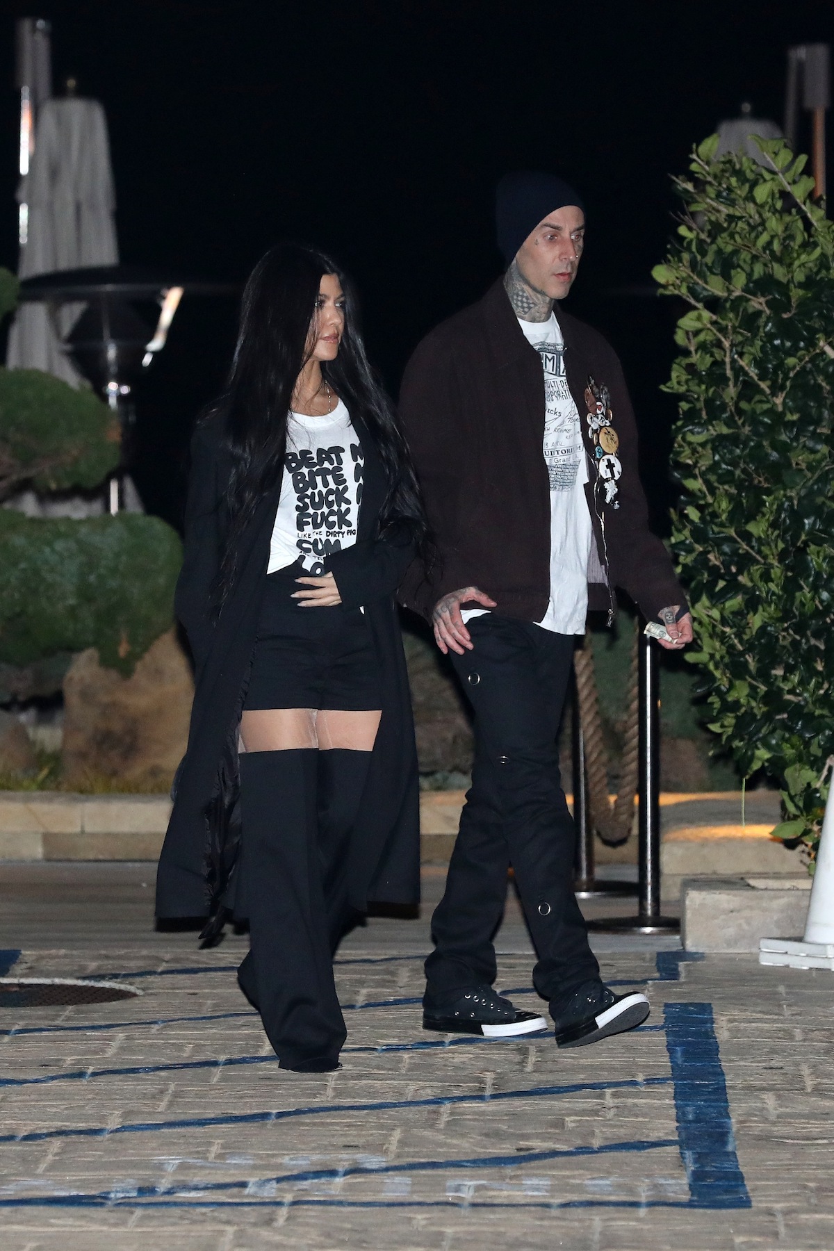 Kourtney Kardashian and Travis Barker walk down a street together holding hands.