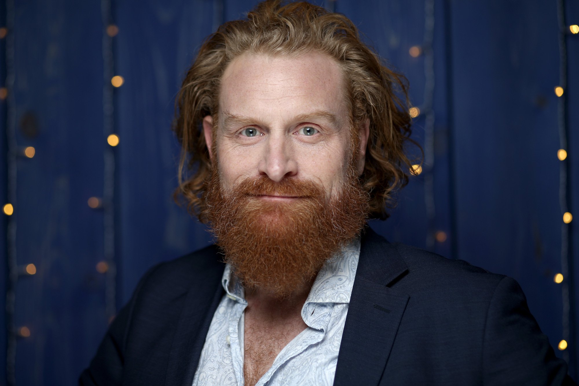 'Game of Thrones' and 'The Witcher' Season 2 star Kristofer Hivju. He's wearing a white button-up shirt and black jacket, and his red hair is slicked back.