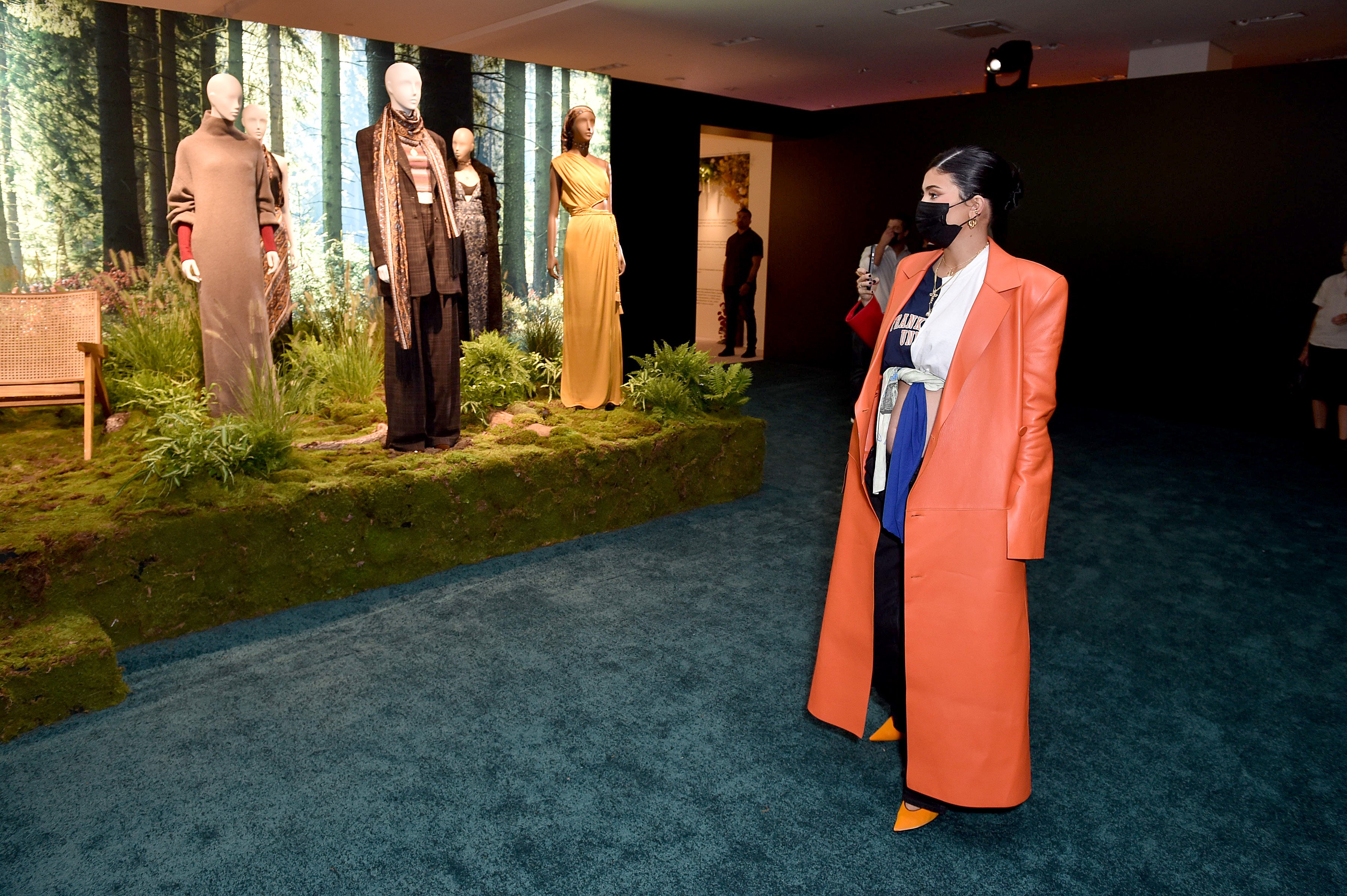 Kylie Jenner flaunting her second pregnancy while wearing an orange trench coat, crop top, and pants.