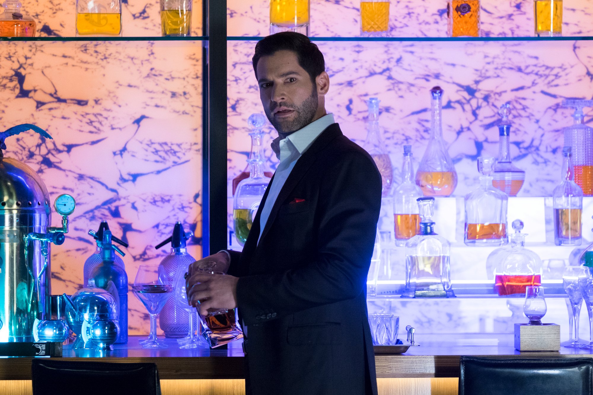 A shot of Tom Ellis as Lucifer Morningstar in 'Lucifer' Season 4. He's standing in front of a bar and holding a drink. 'Lucifer' Season 2 set up many of the storylines the show's later episodes would cover.