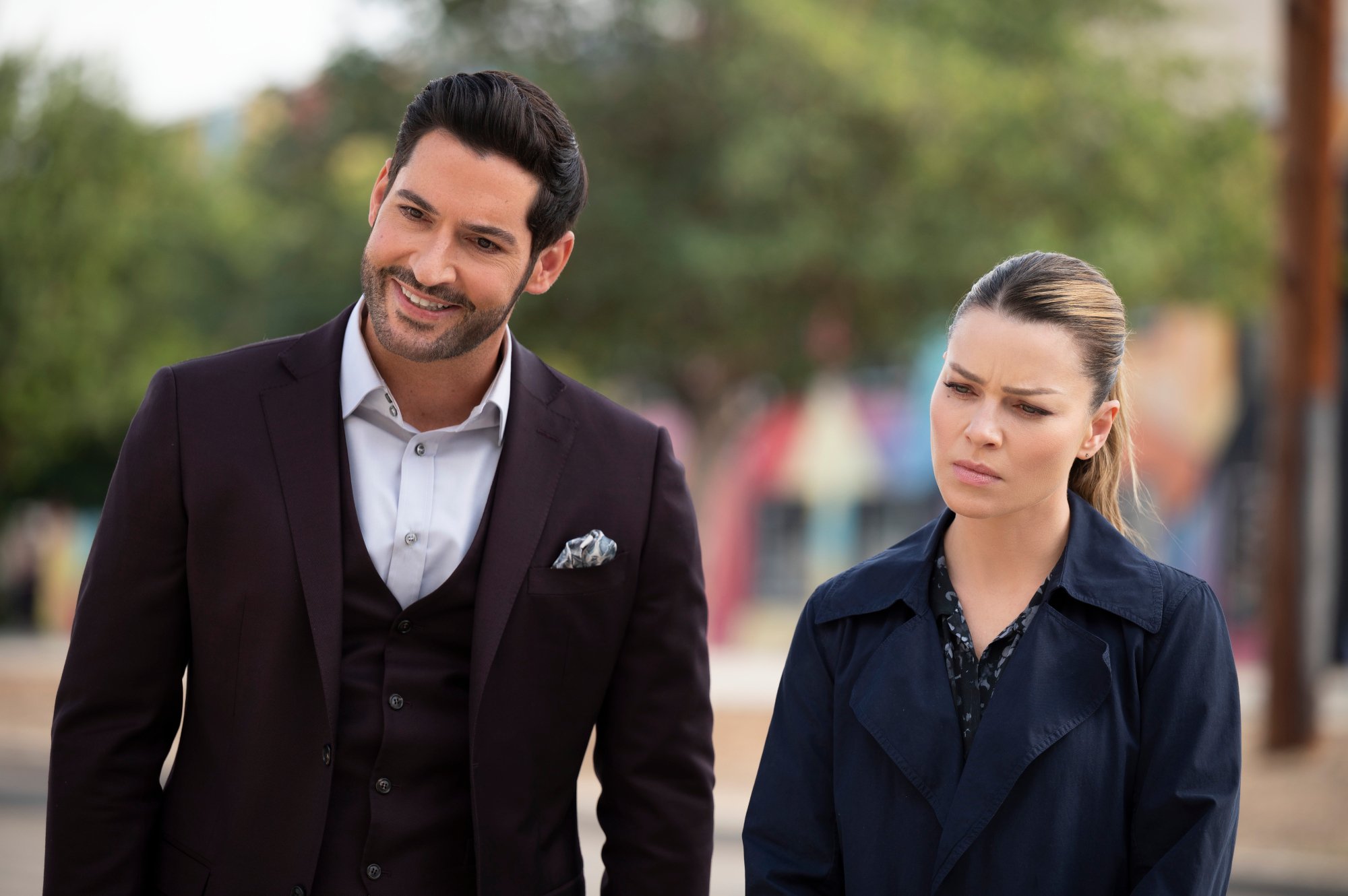 Tom Ellis and Lauren German in one of the episodes in 'Lucifer' Season 6. He's wearing a suit and smiling, and she has a concerned look on her face.