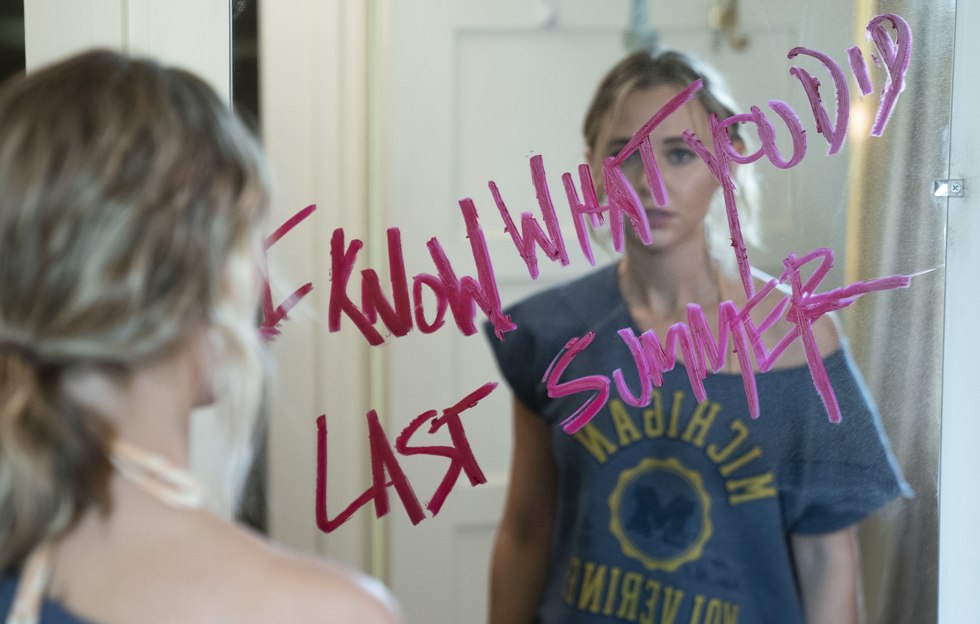 Madison Iseman standing in front of a mirror with lipstick on it in 'I Know What You Did Last Summer' Amazon Prime series.