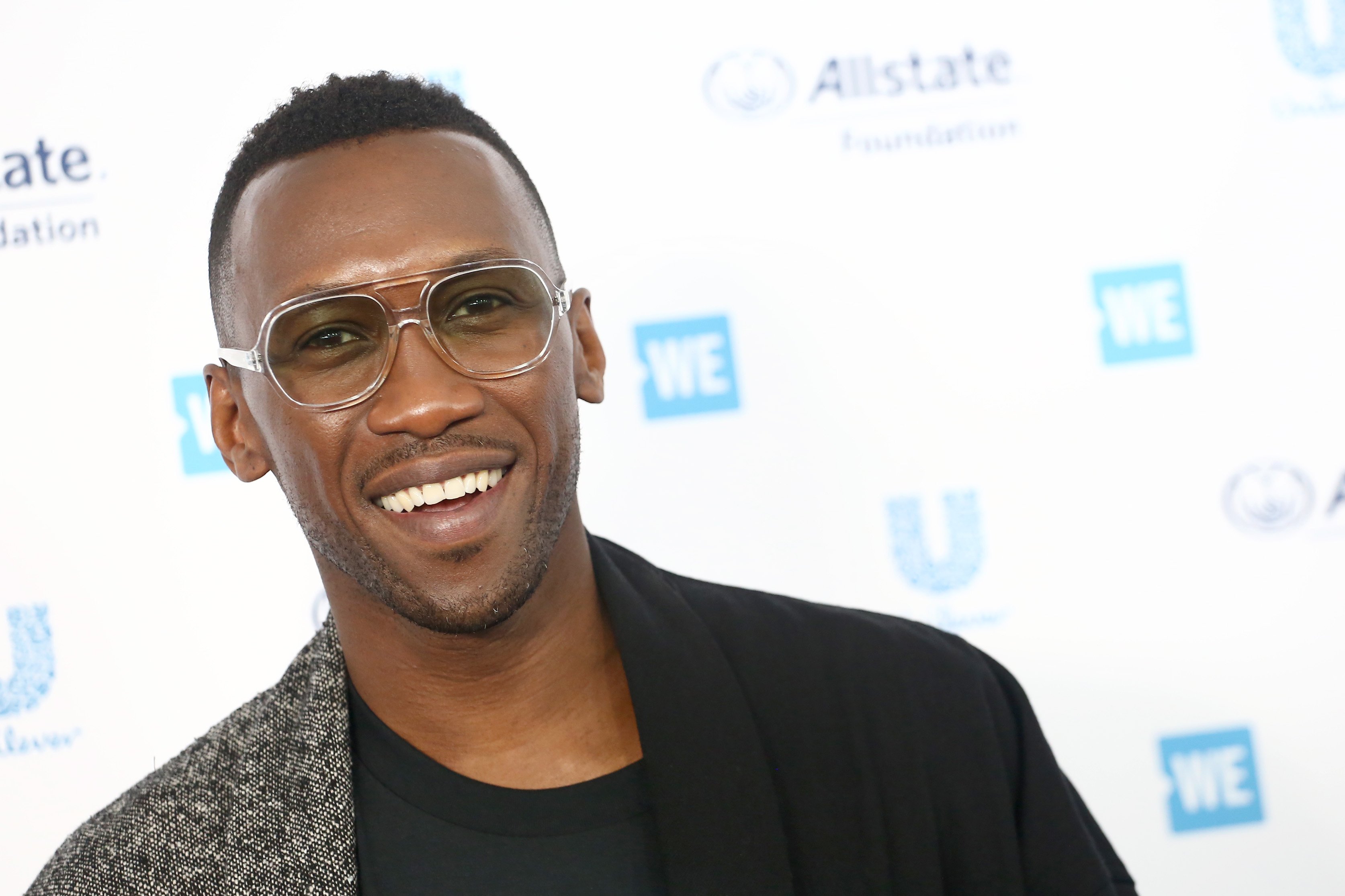 Mahershala Ali in a black t-shirt and dual colored brown and black jacket at an event in 2019.