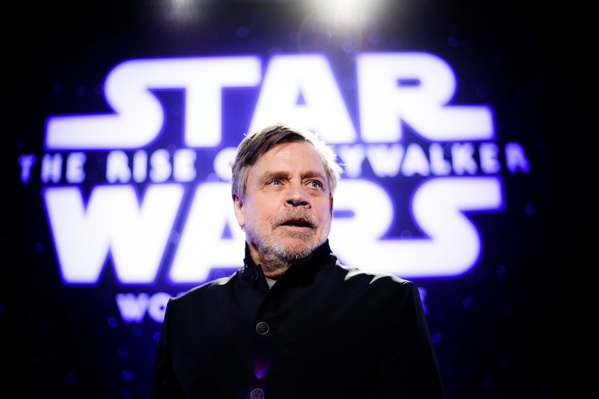 Mark Hamill smiling in front of a 'Star Wars' logo