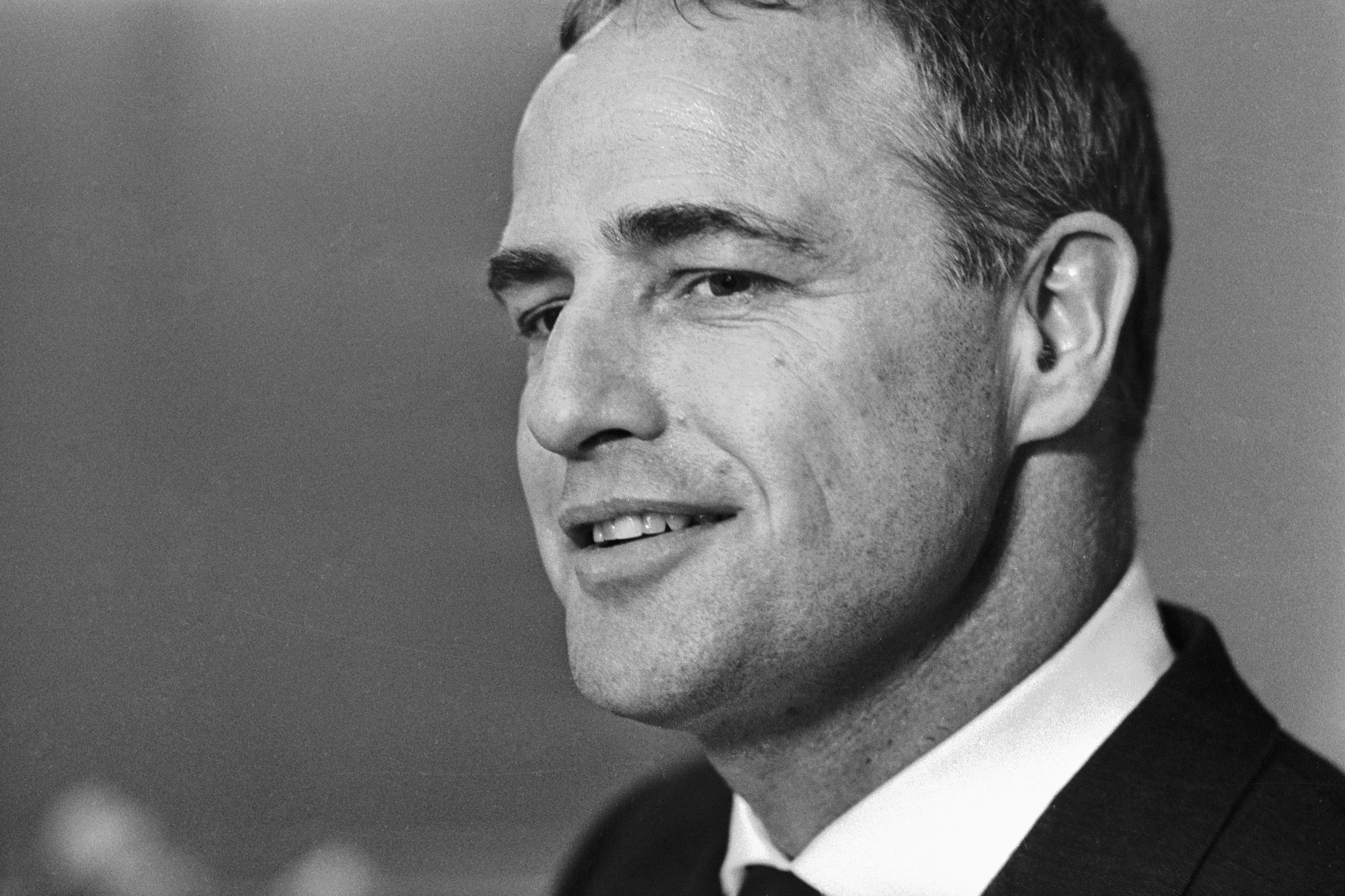 Marlon Brando smiling, wearing a suit in a black and white photo.