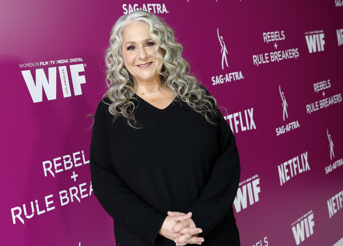 Grace and Frankie Executive Producer Marta Kauffman smiles for a photo. She is wearing a black dress and her curly grey hair is down.