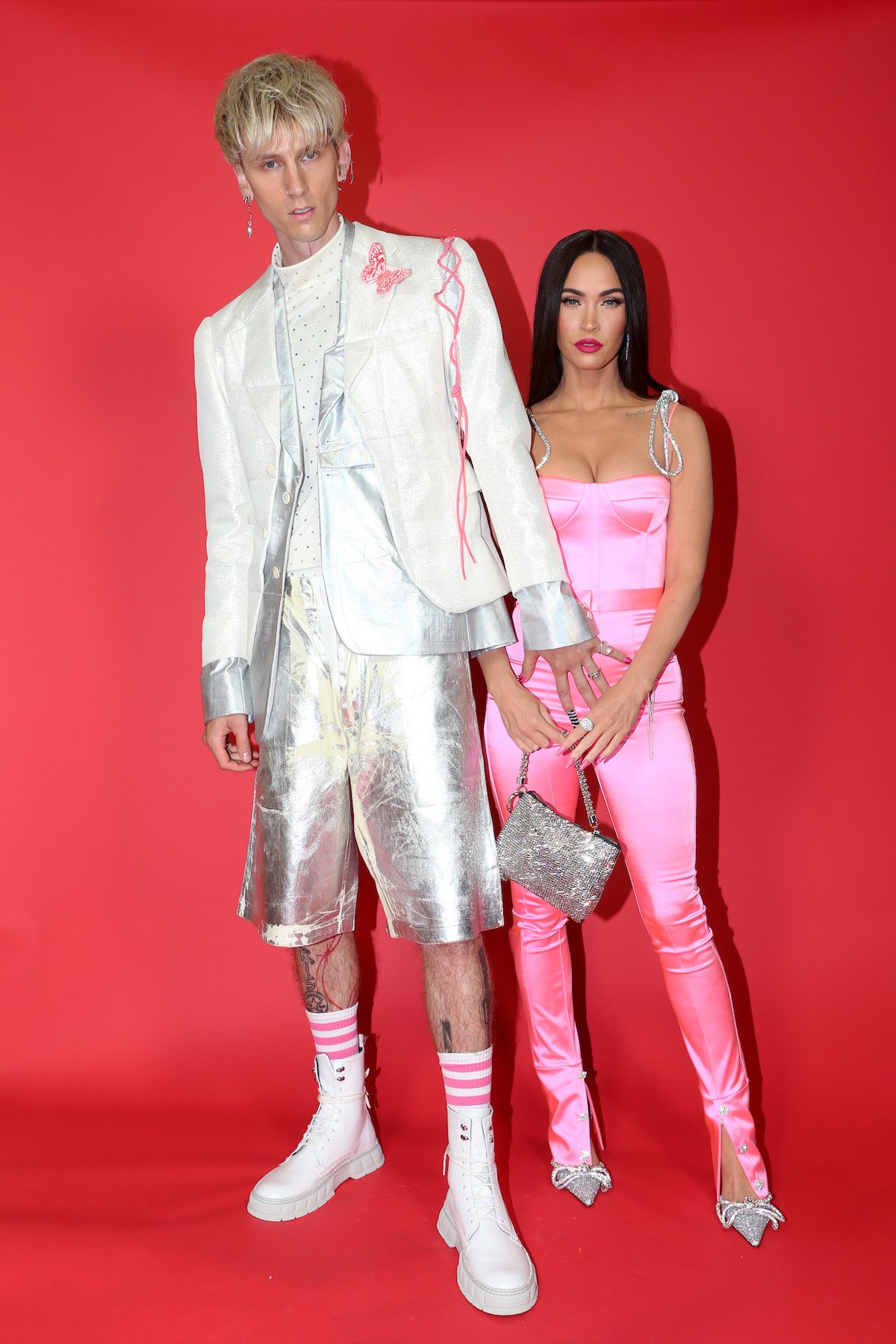 Machine Gun Kelly and Megan Fox pose together in front of a red background at an event.