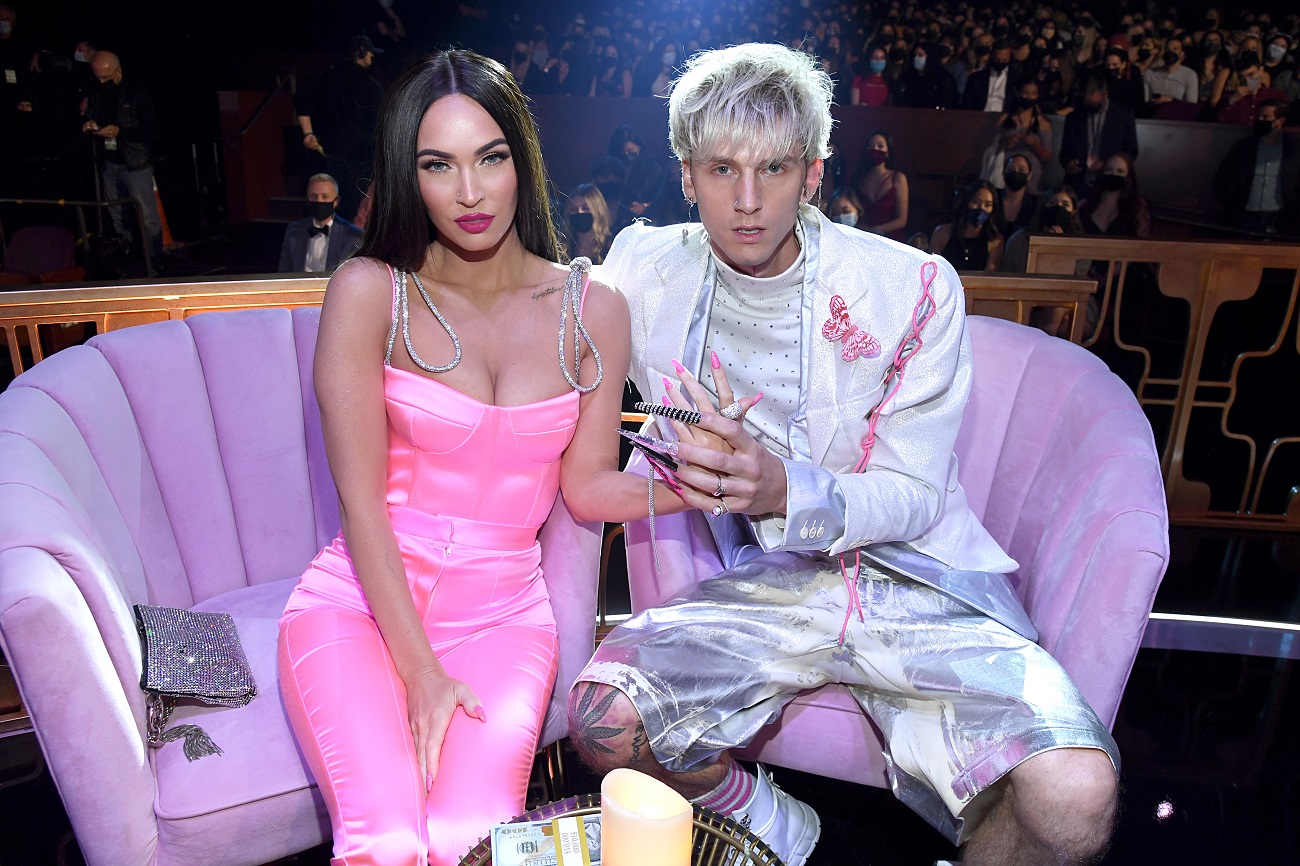 Megan Fox and Machine Gun Kelly sit together on a lavender colored couch.