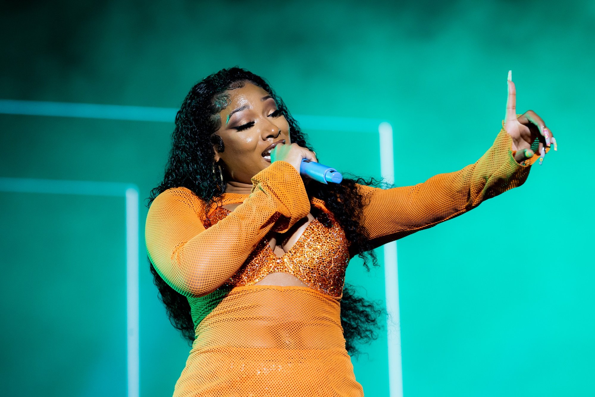 Megan Thee Stallion performing on stage in a bright orange outfit