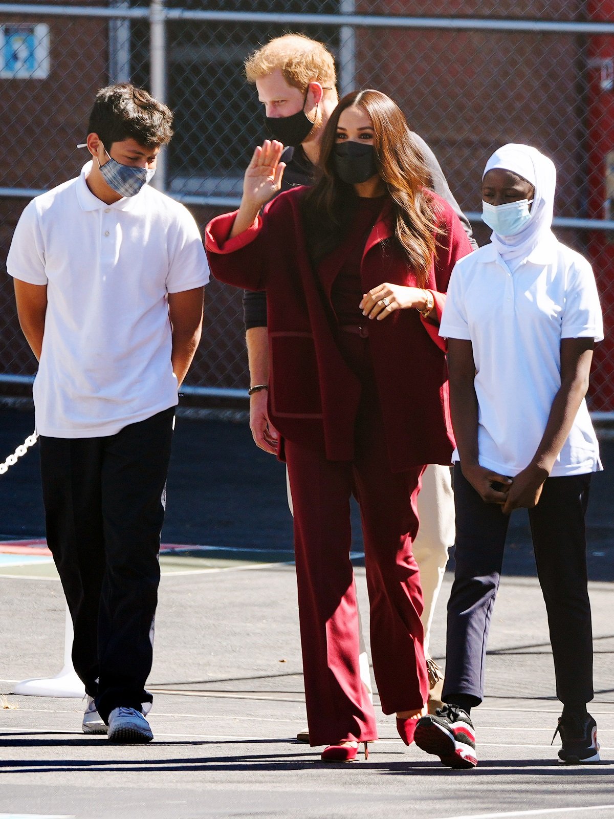 Meghan Markle and Prince Harry walking with two kids outdoors with the Duchess of Sussex waving and the Duke of Sussex behind her