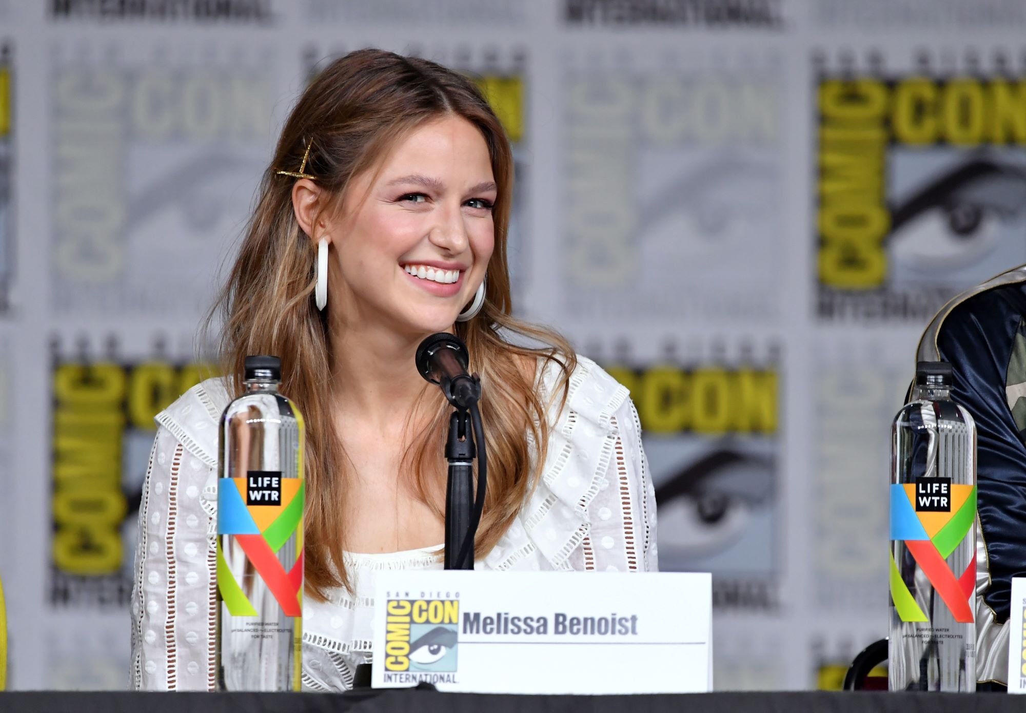 'Supergirl' Season 6 Episode 13 star Melissa Benoist wear a long sleeved white blouse and speaks onstage at Comic-Con.