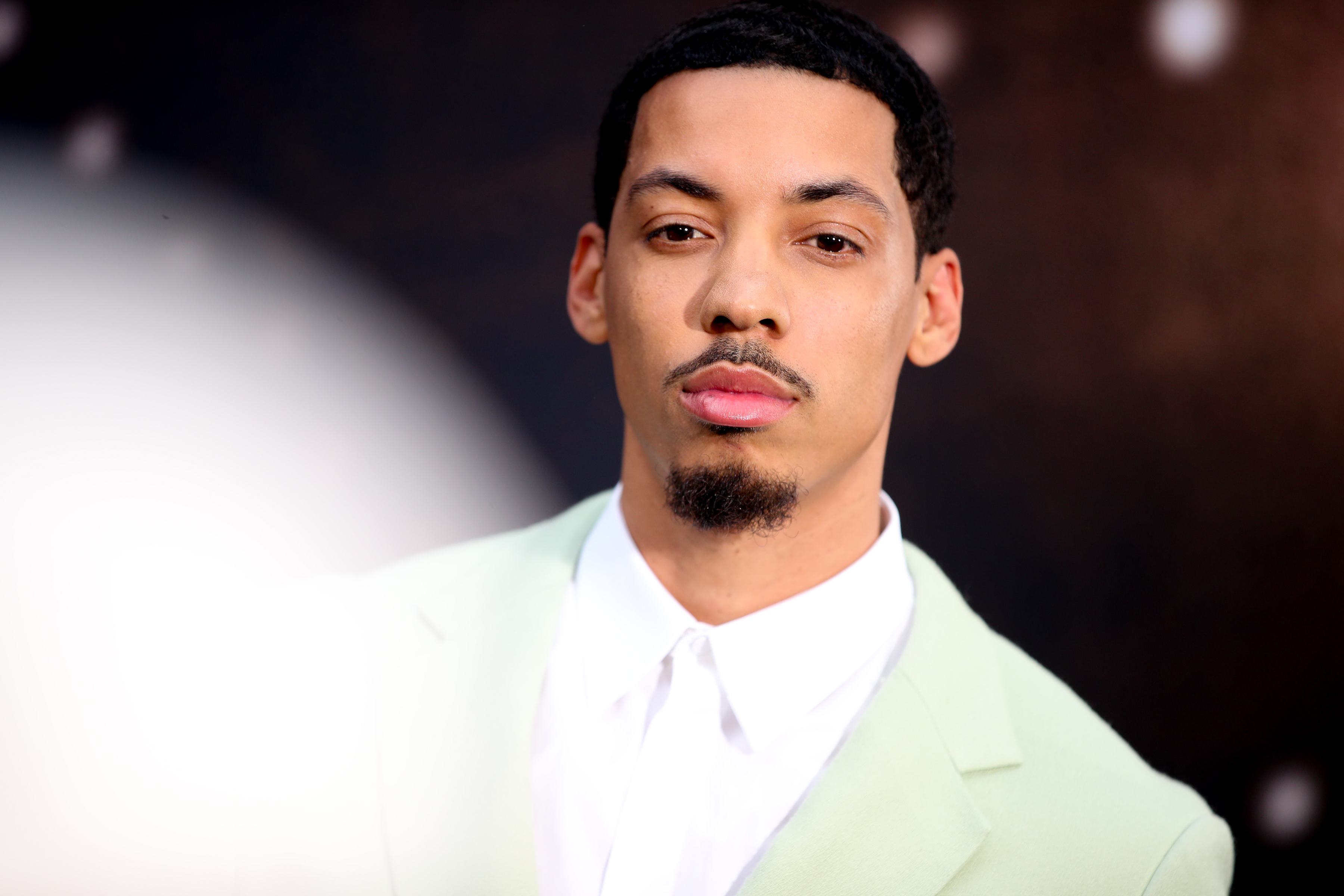 Melvin Greg poses for a photo without smiling, wearing a green suit and tie. 