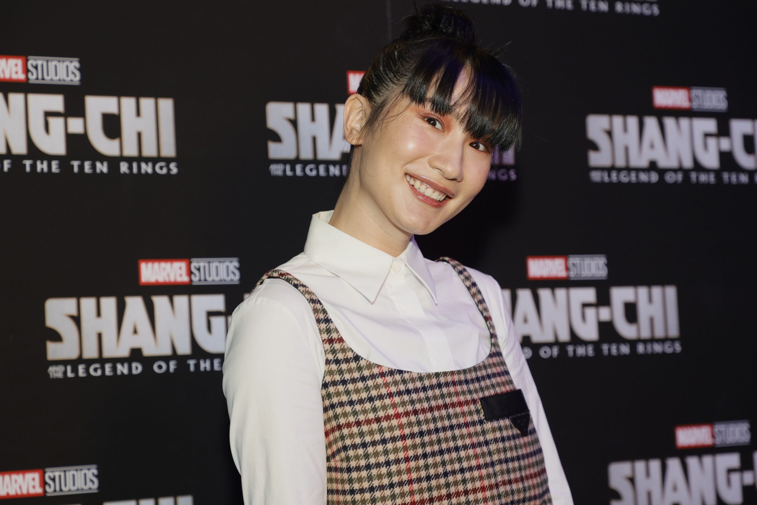 Meng'er Zhang, in a white shirt and checkered dress, smiling at the camera at a screening for her movie 'Shang-Chi and the Legend of the Ten Rings.'